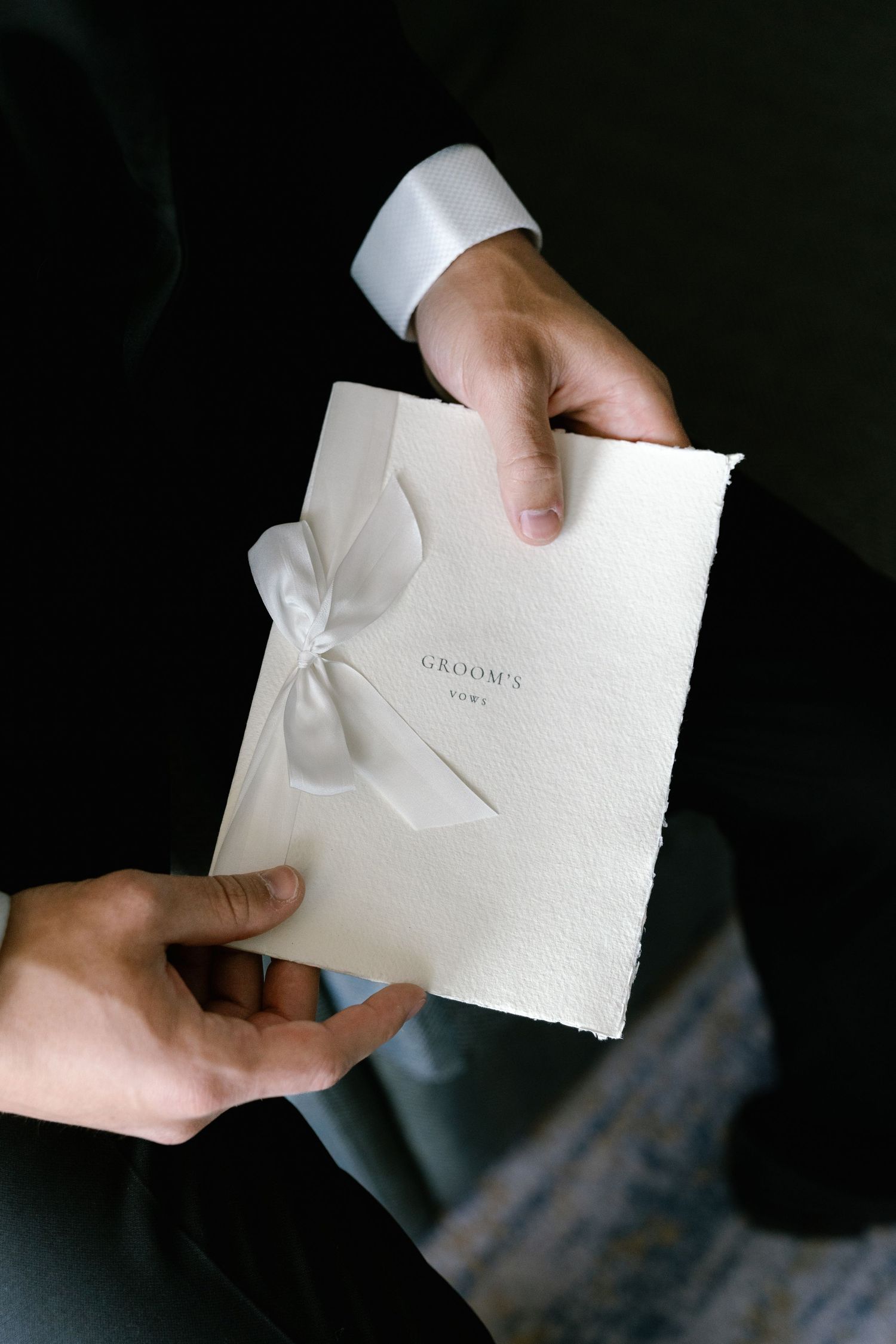 Hands holding elegant white wedding invitation envelope against dark background.