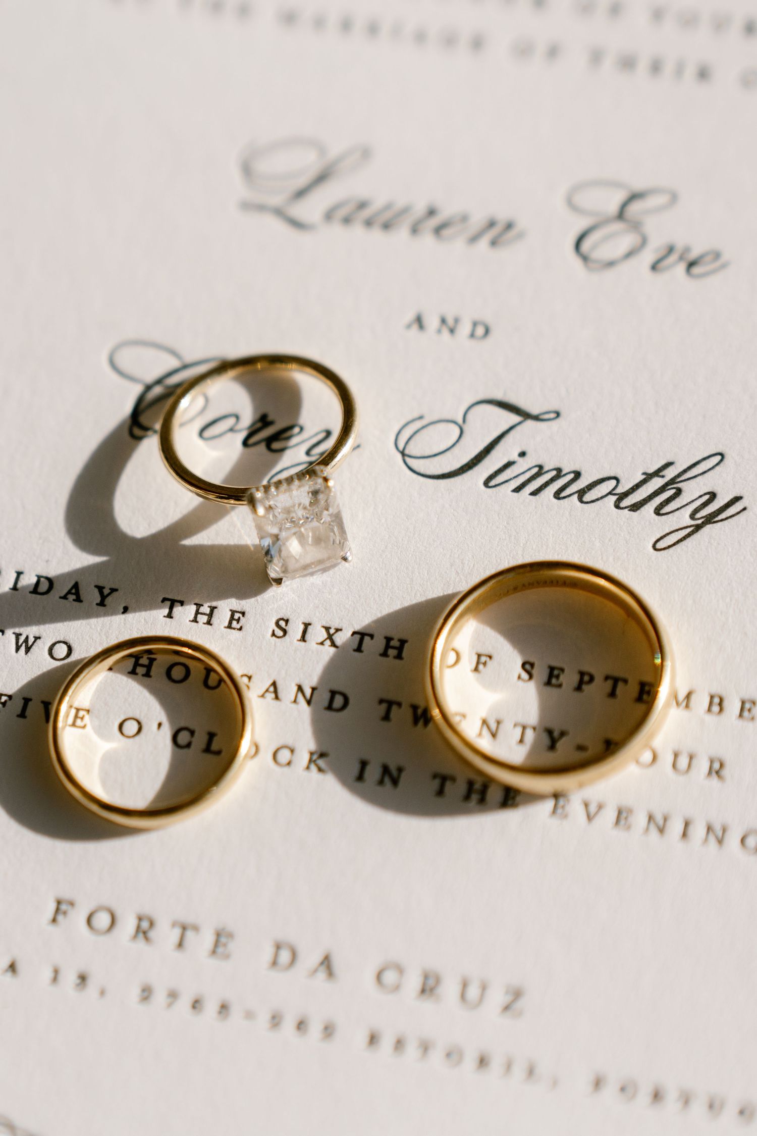 Gold wedding rings casting shadows on elegant wedding invitation text.