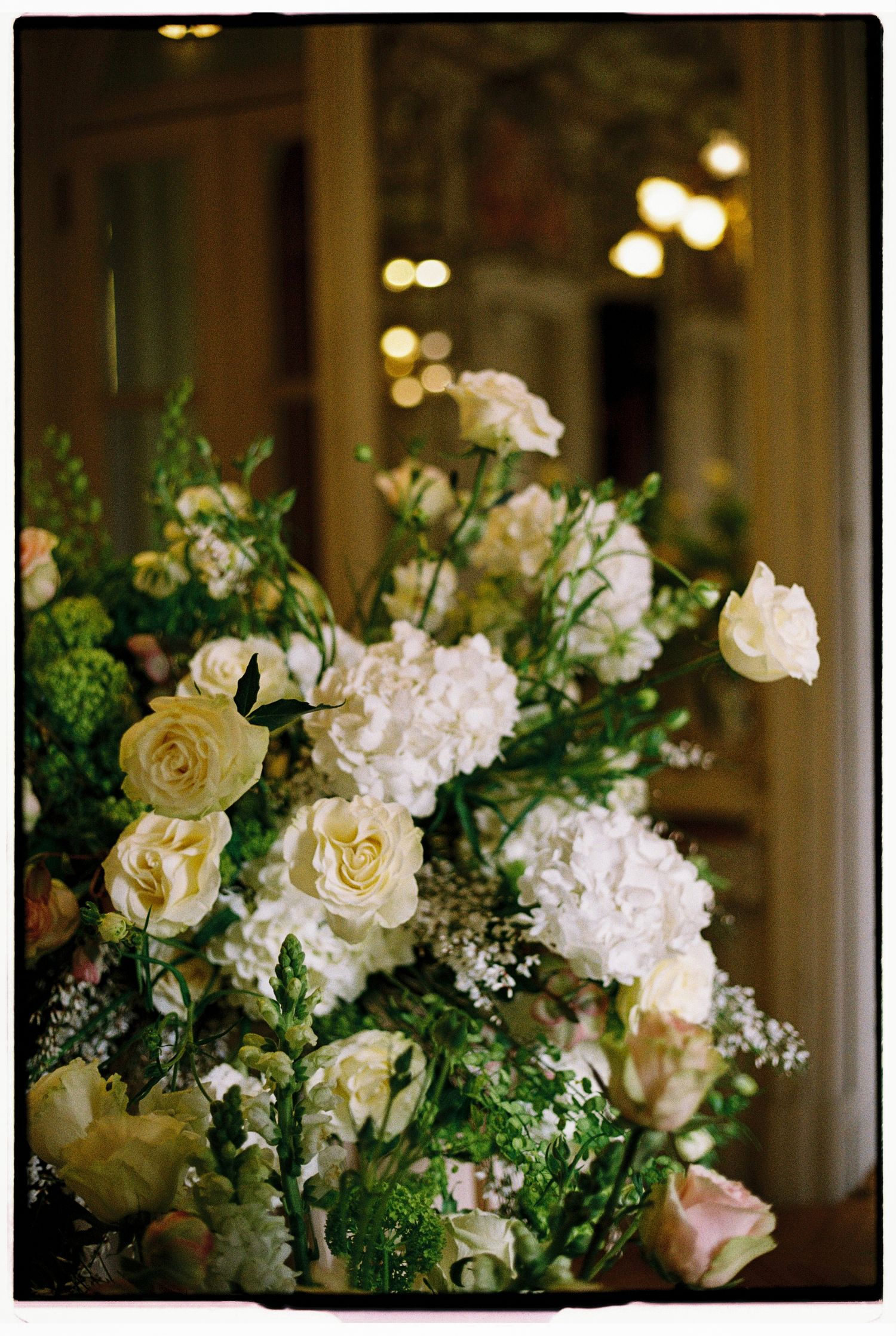 Lush wedding floral arrangement featuring white hydrangeas, cream roses, and greenery in an elegant indoor setting.