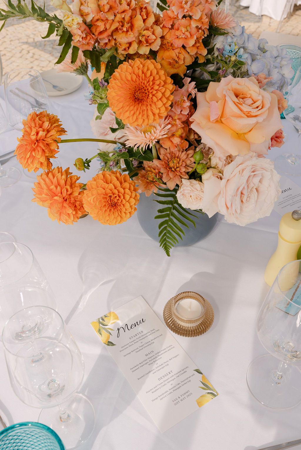 Wedding reception table decorated with coral dahlias, peach roses, and elegant place settings.