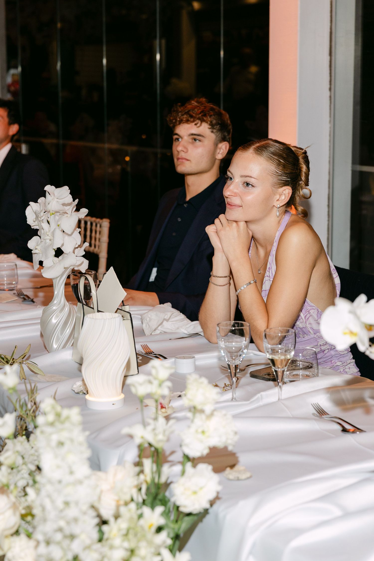 Wedding reception dinner table with white floral centerpieces and candlelight.