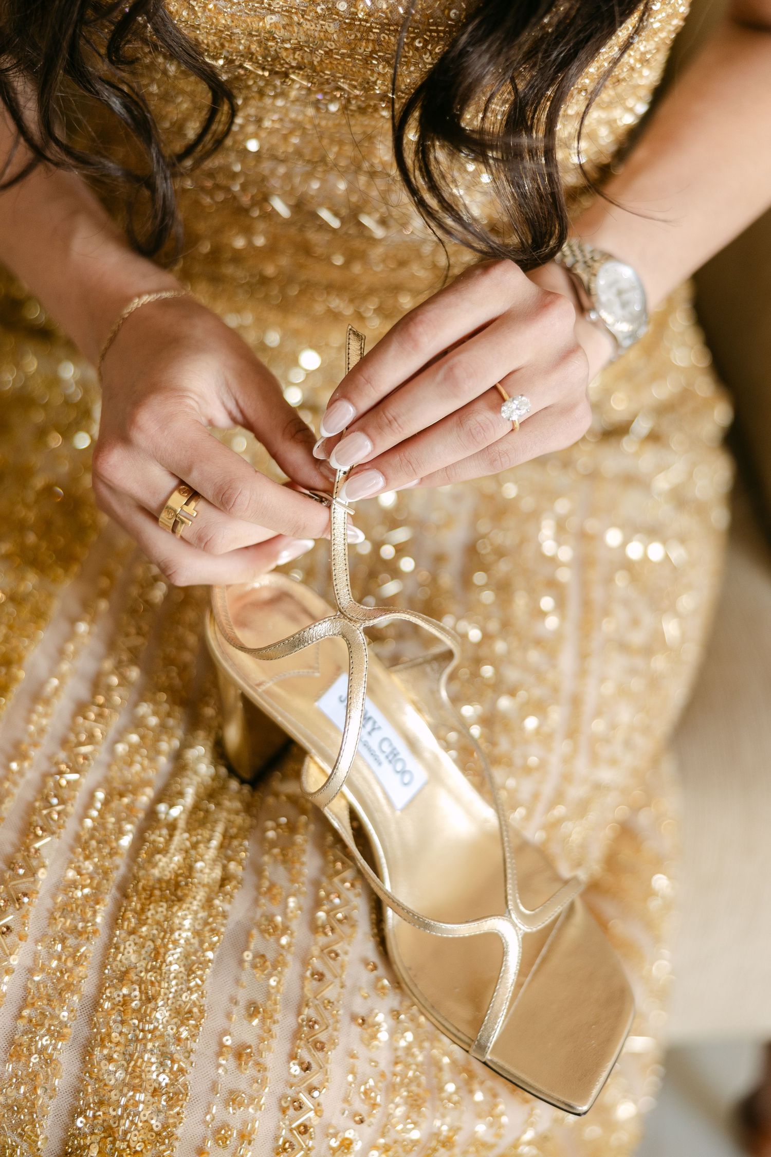 Close-up of hands adjusting a sparkly gold Jimmy Choo shoe strap.