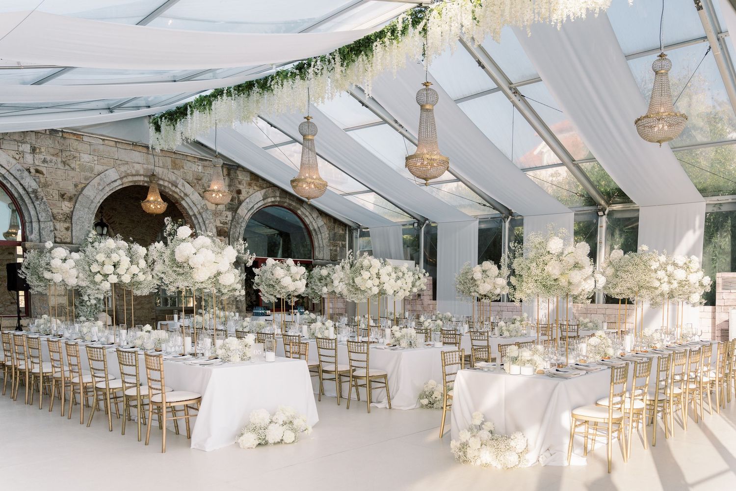 White wedding reception tent decorated with floral arrangements and crystal chandeliers for an elegant celebration.