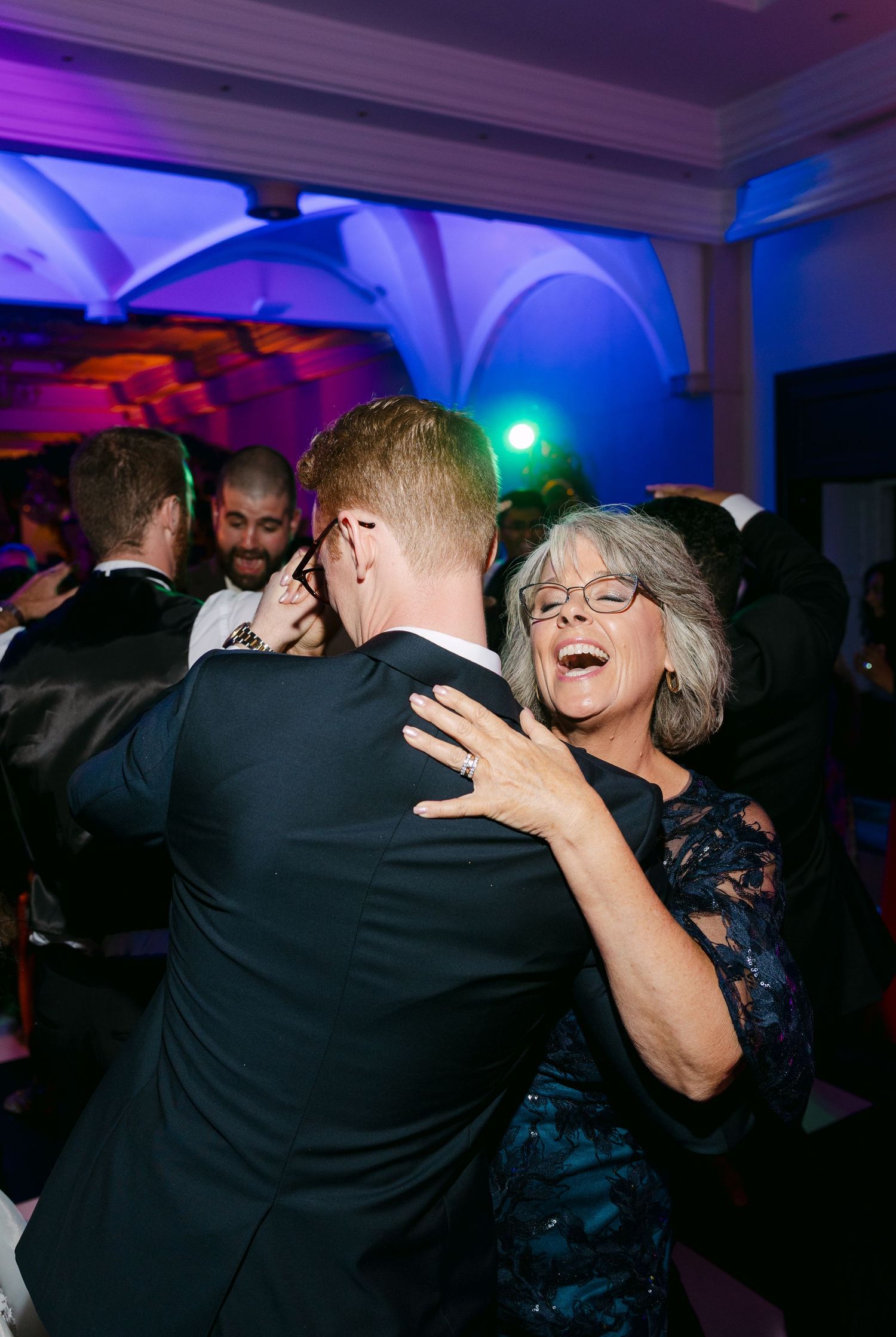 Wedding guests dancing at a reception under dramatic blue and purple lighting.