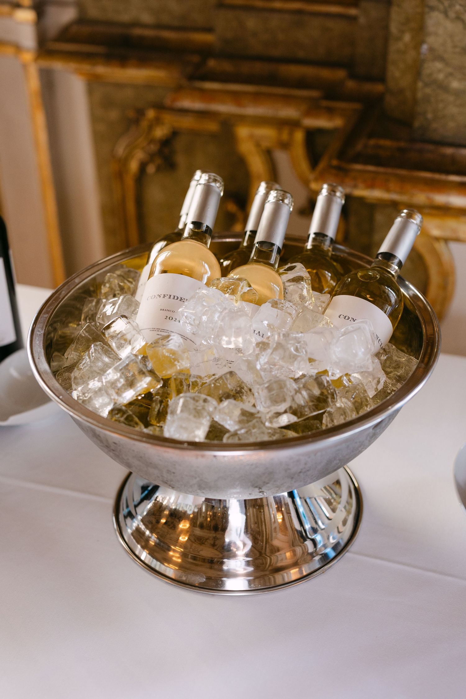 Silver champagne bowl filled with ice and white wine bottles at formal event.