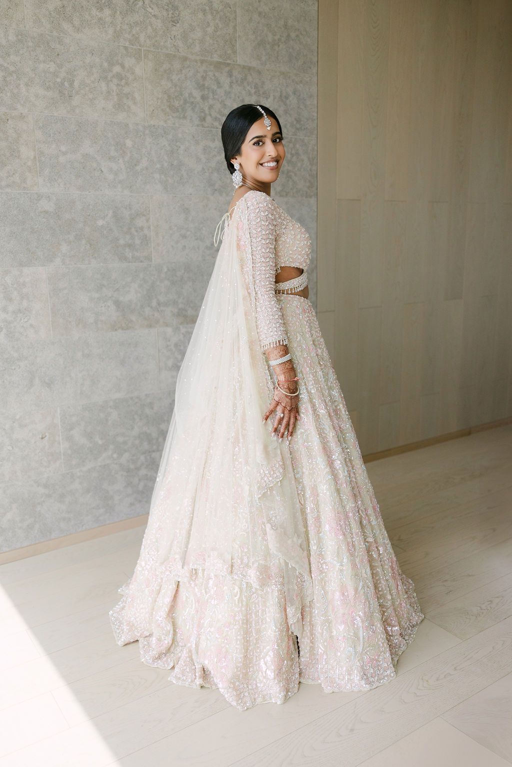 A bride twirls in an elegant white sequined lehenga against a neutral indoor backdrop.