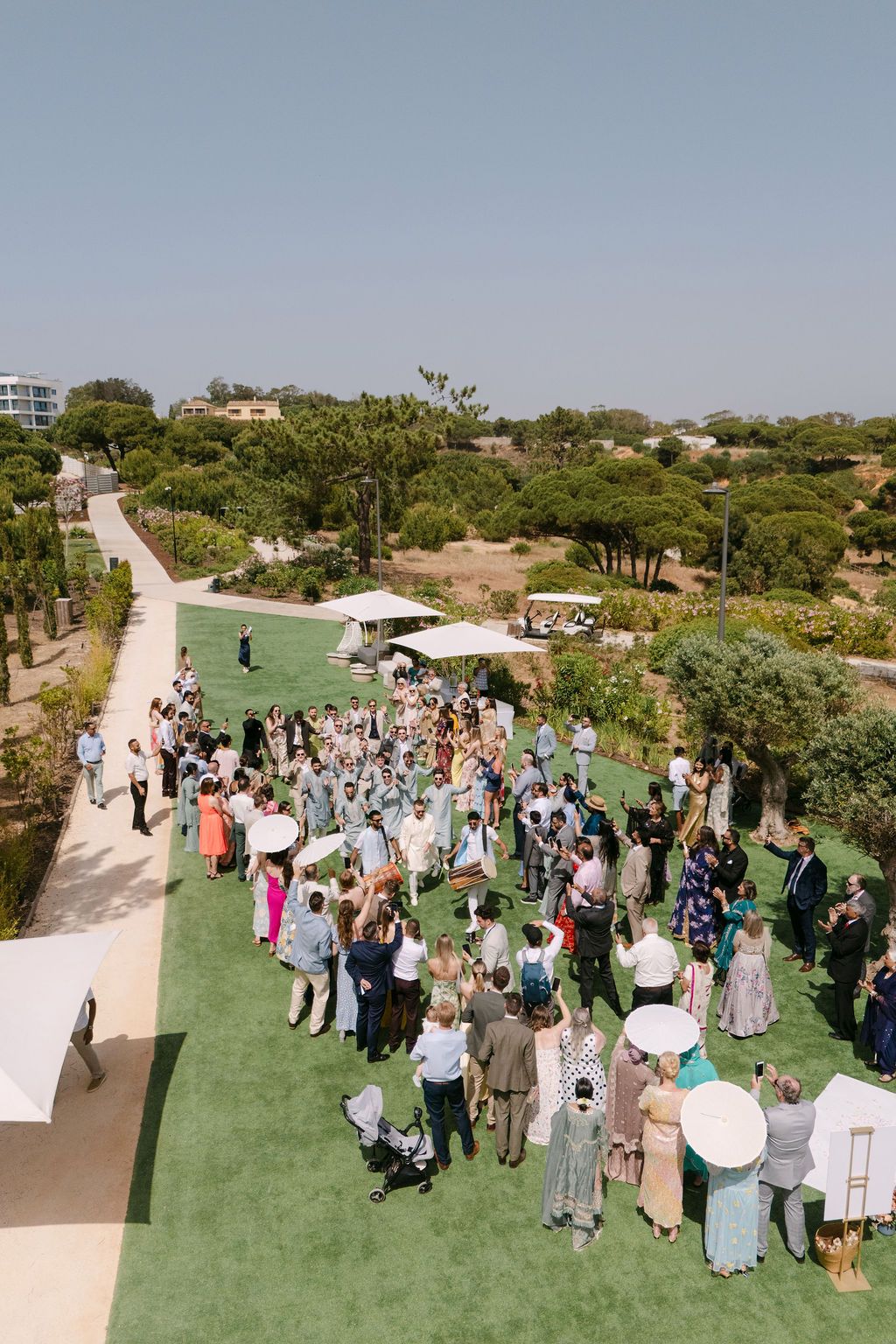 Aerial view of wedding guests mingling on a green lawn during an outdoor reception.