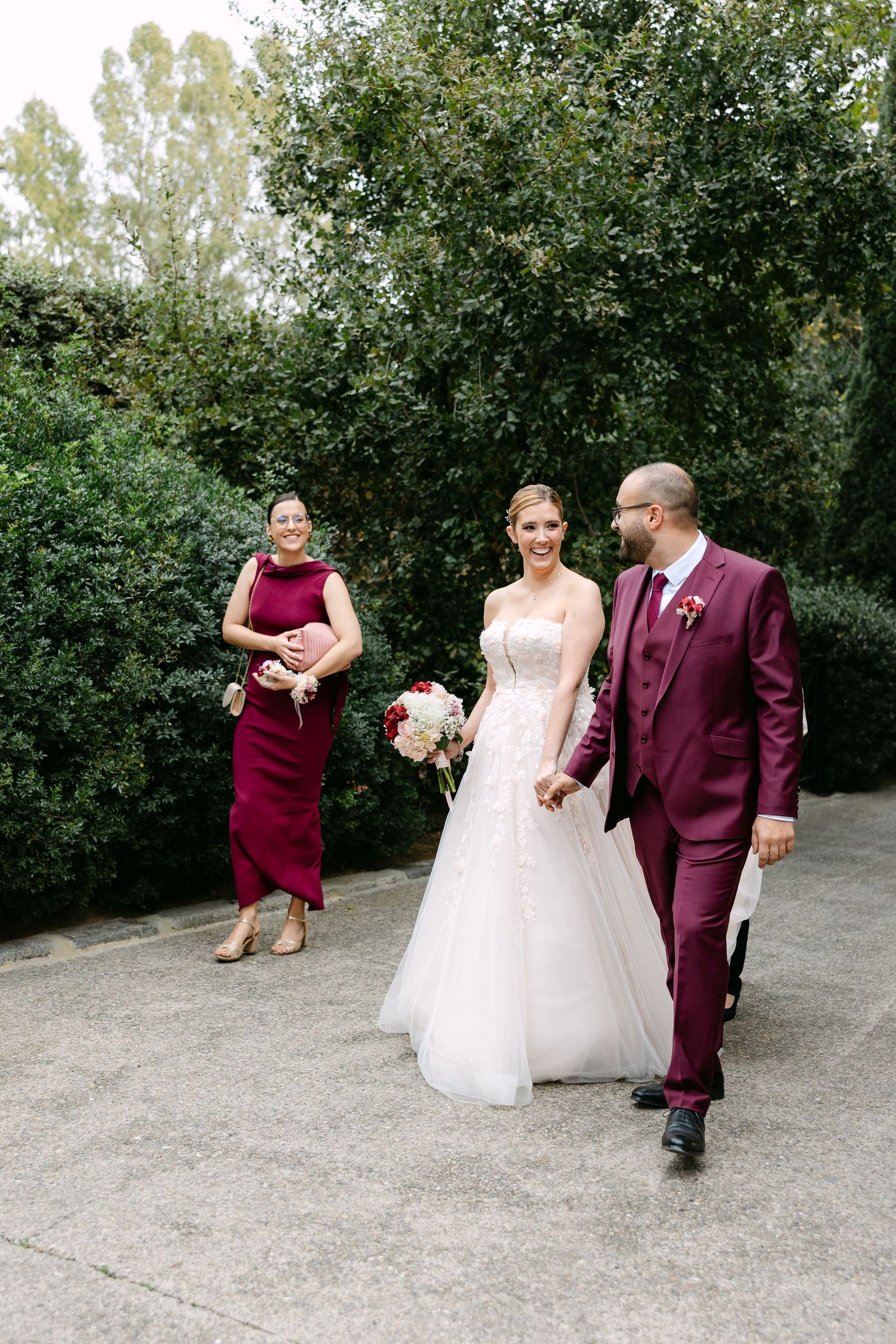 Wedding party poses outdoors with burgundy and white attire against a natural backdrop.