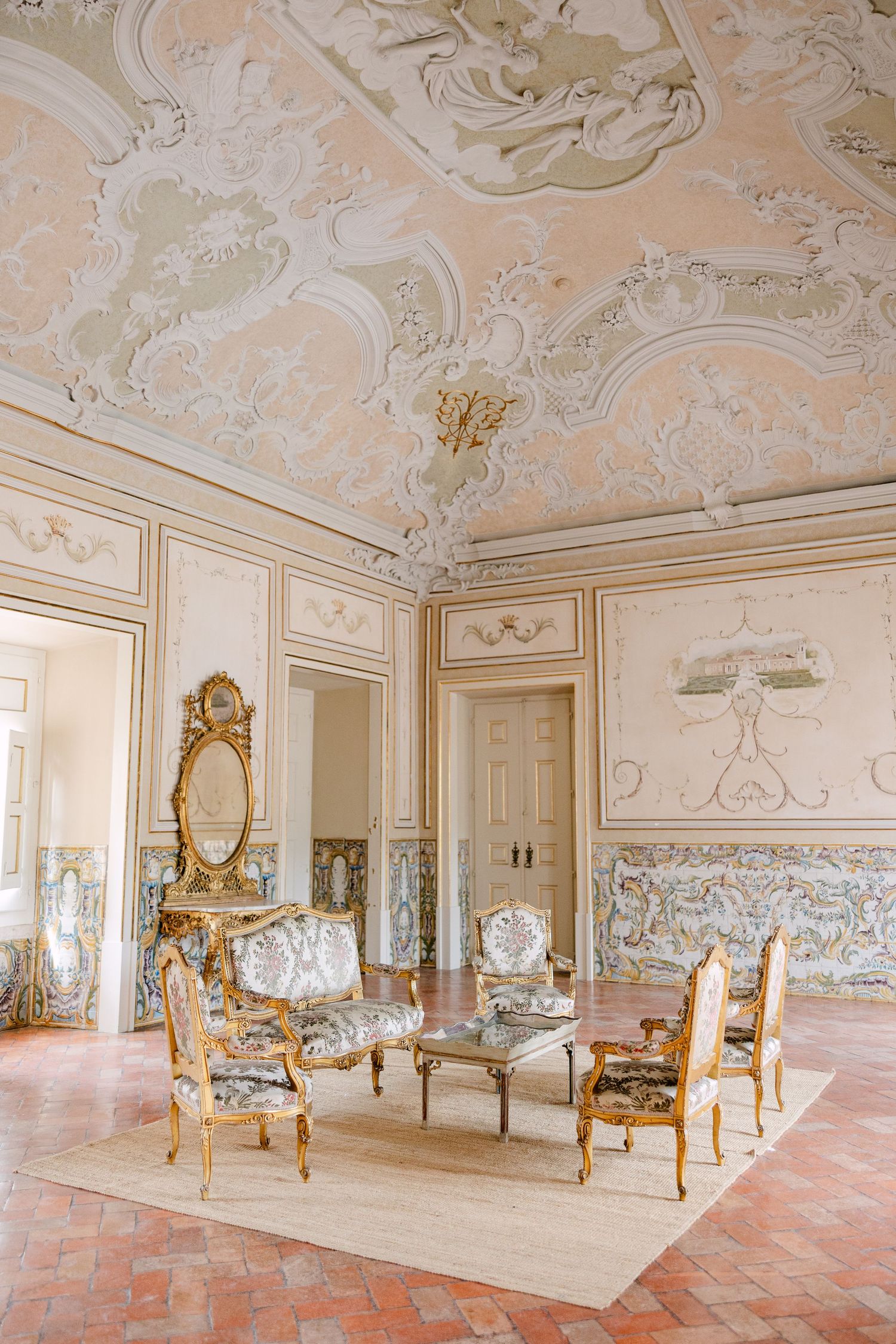 Ornate baroque room with decorative ceiling, gilded mirrors and antique furniture in a palatial setting.