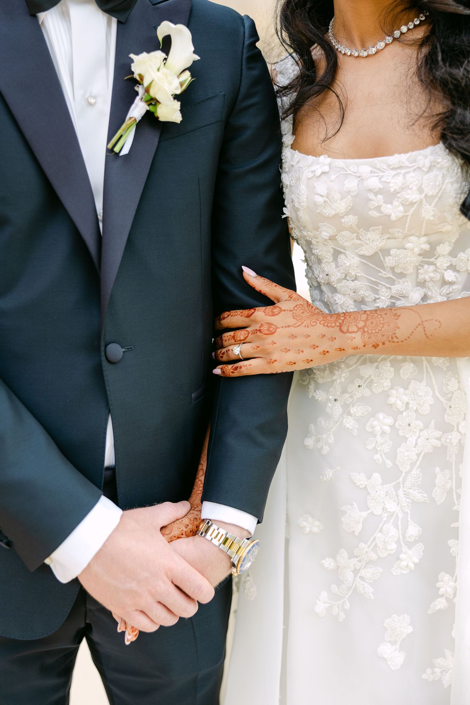 Close-up detail of wedding attire showing white boutonniere, navy suit, and lace bridal gown.