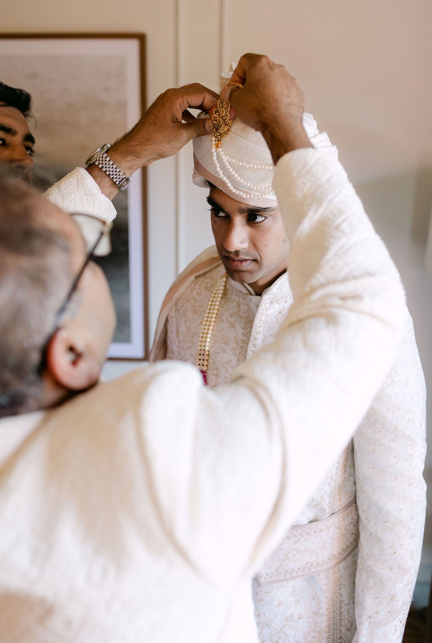 Groom adjusts traditional white Indian wedding attire and pearl necklace.