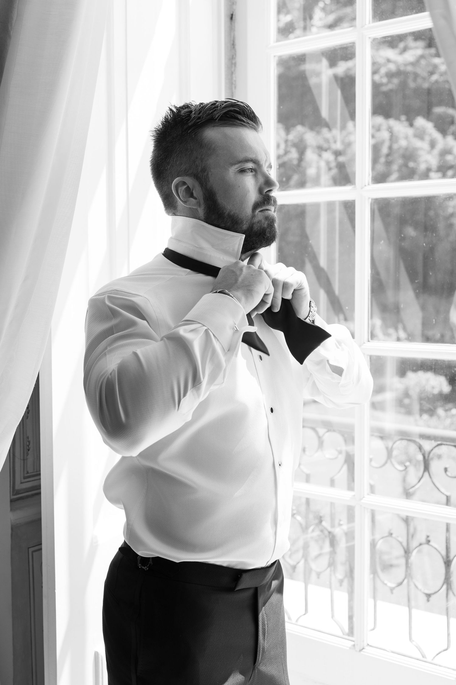 Black and white series of a groom adjusting his tie while getting ready.