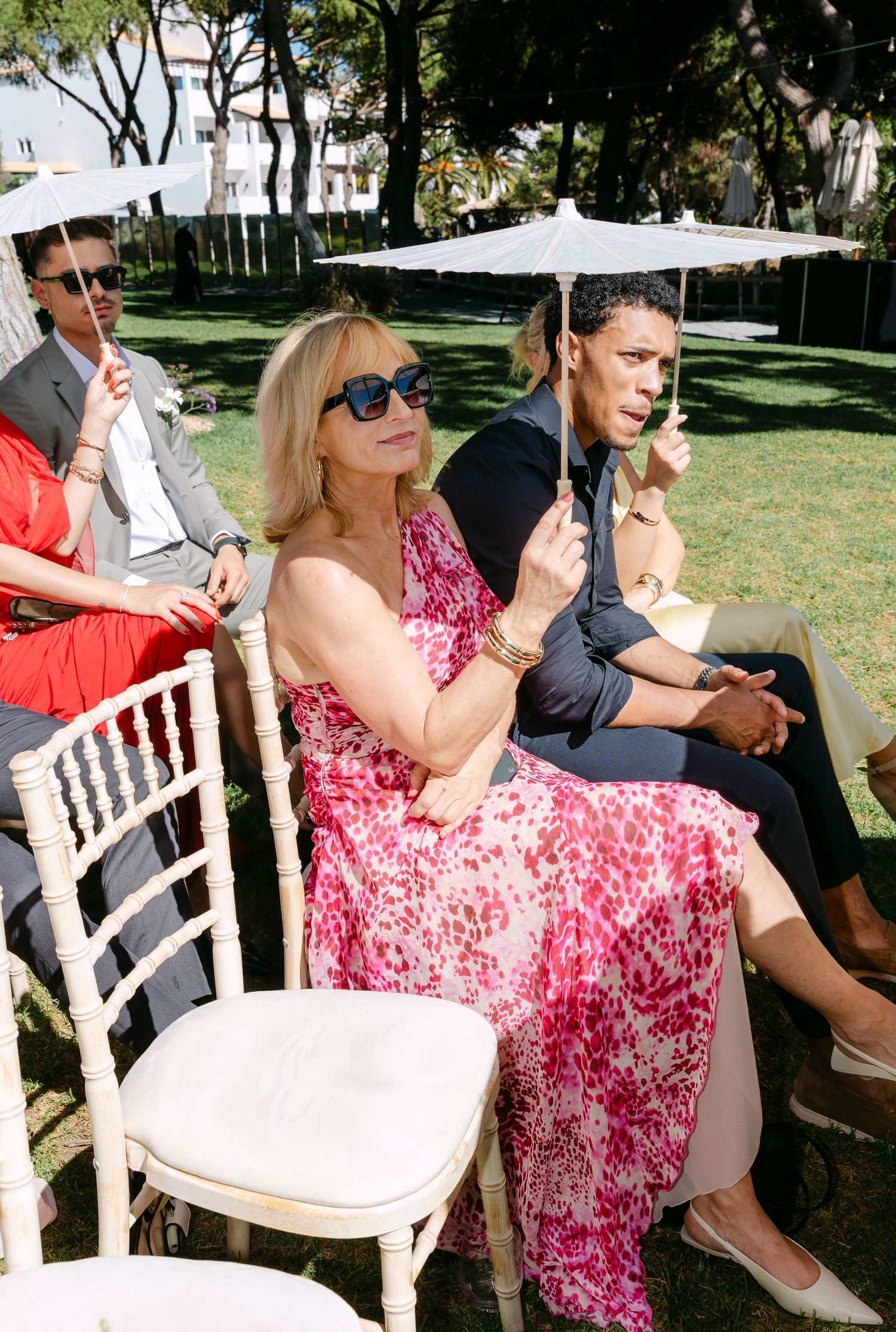 Wedding guests seated in white chairs outdoors wearing summer attire.