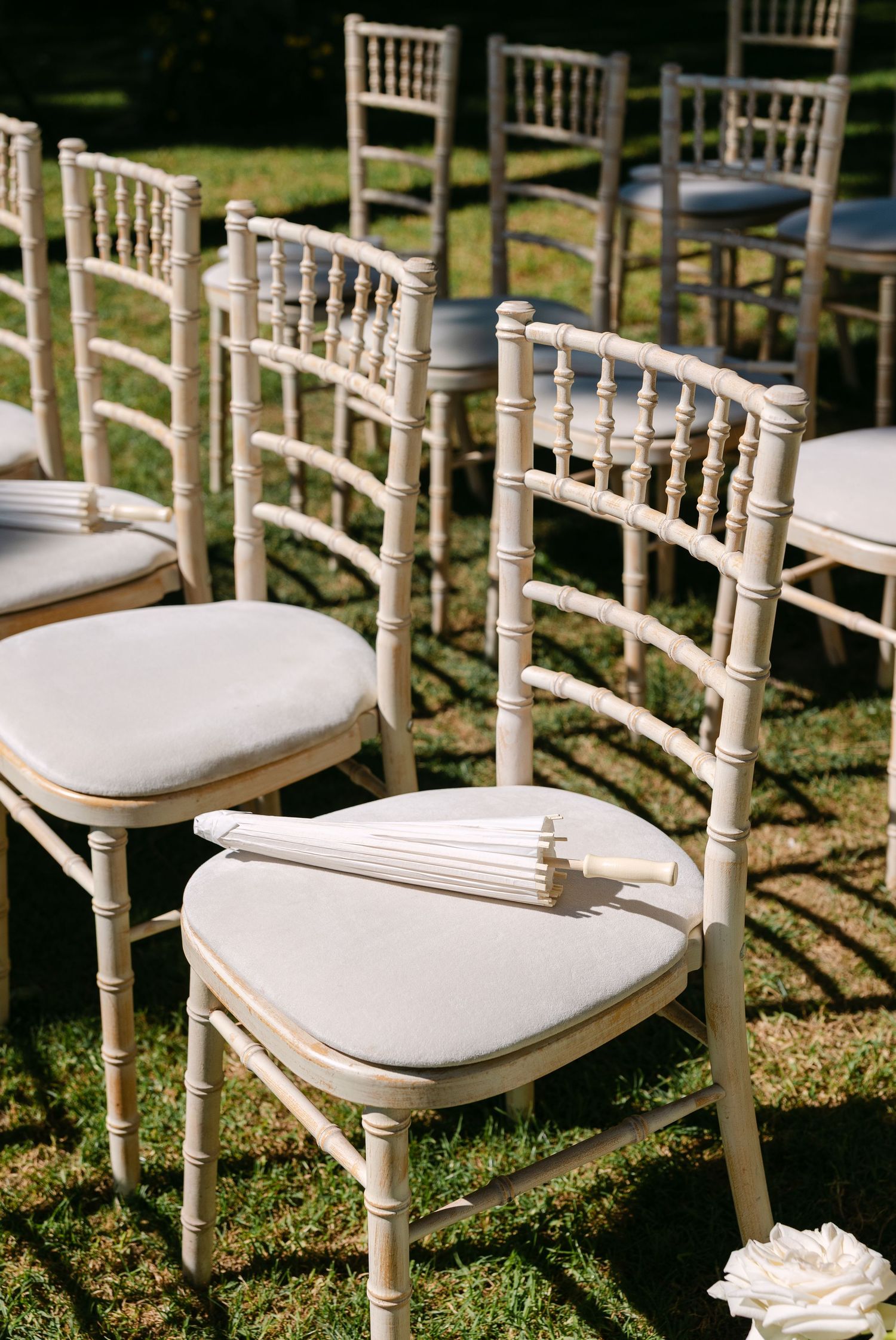 White Chiavari chairs arranged in rows on grass for an outdoor wedding ceremony.