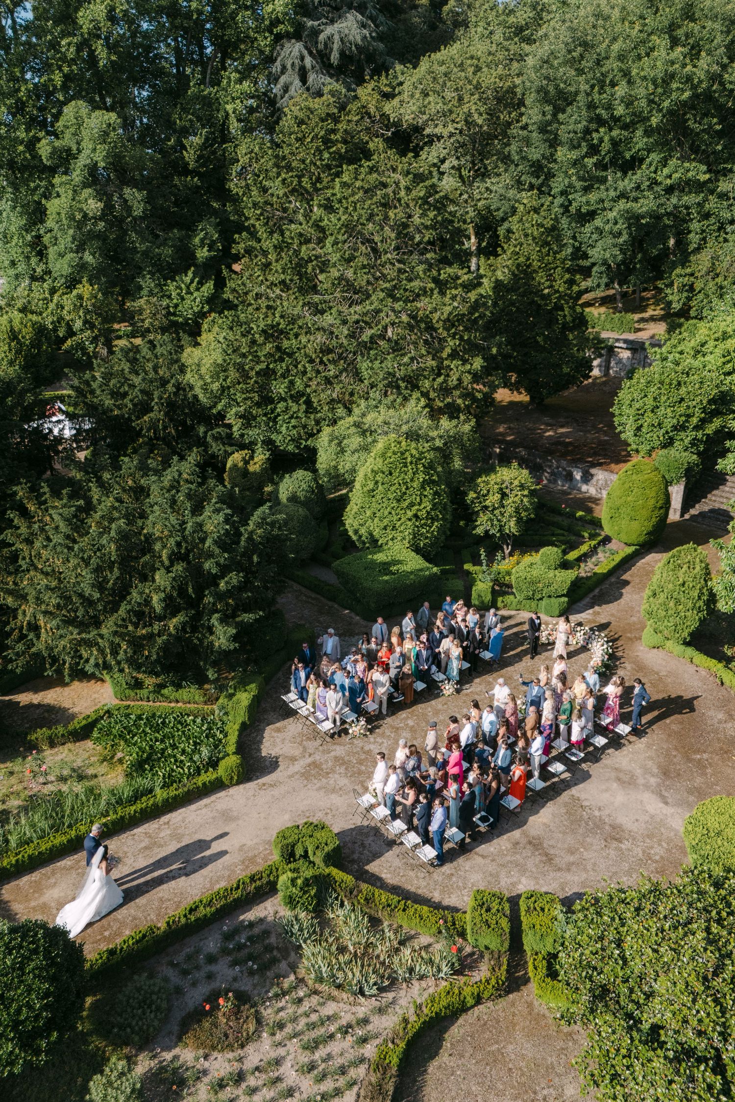 Aerial view of wedding guests gathered in a formal garden surrounded by manicured hedges.