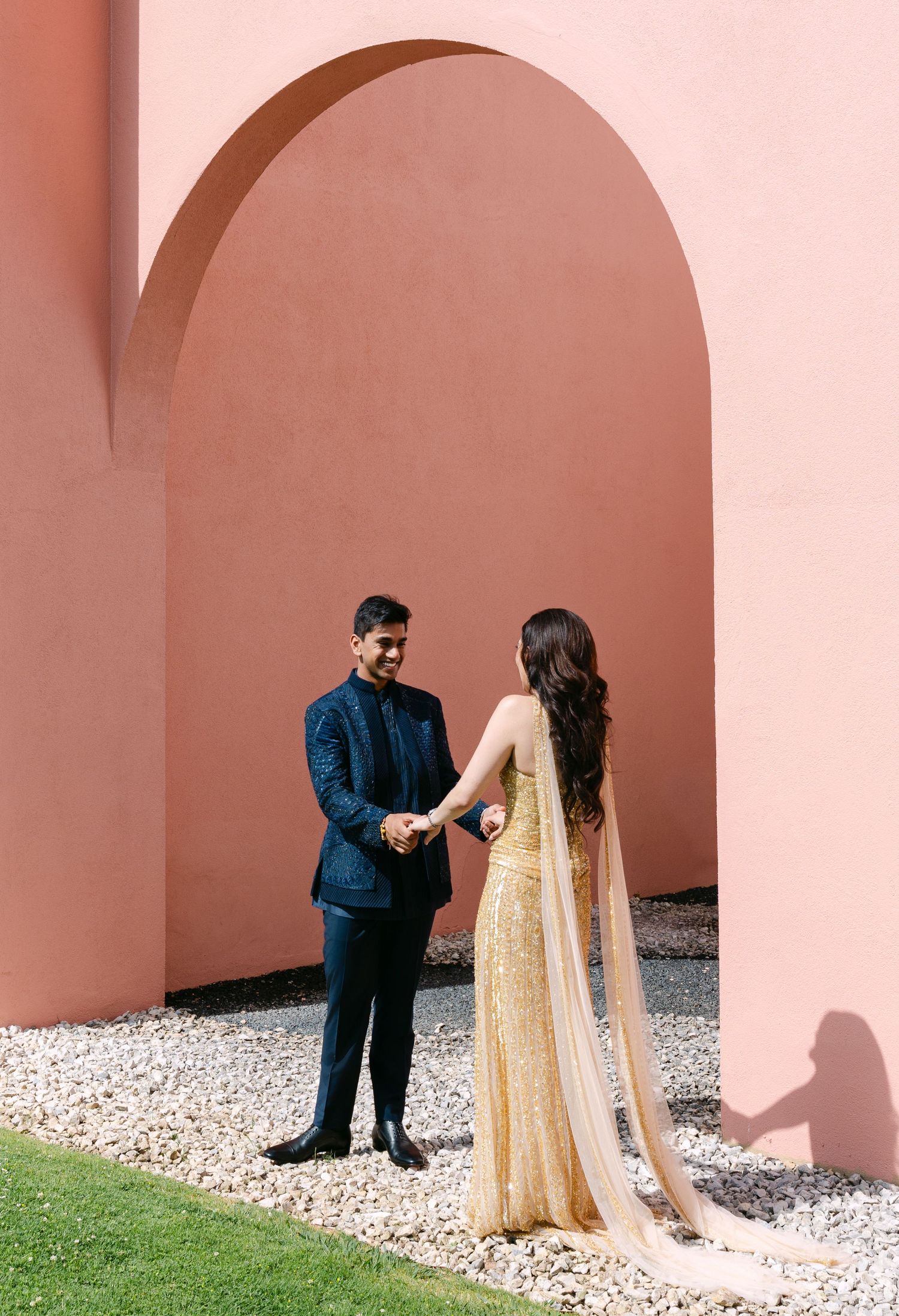 Elegant couple shares intimate moment framed by pink architectural arch.
