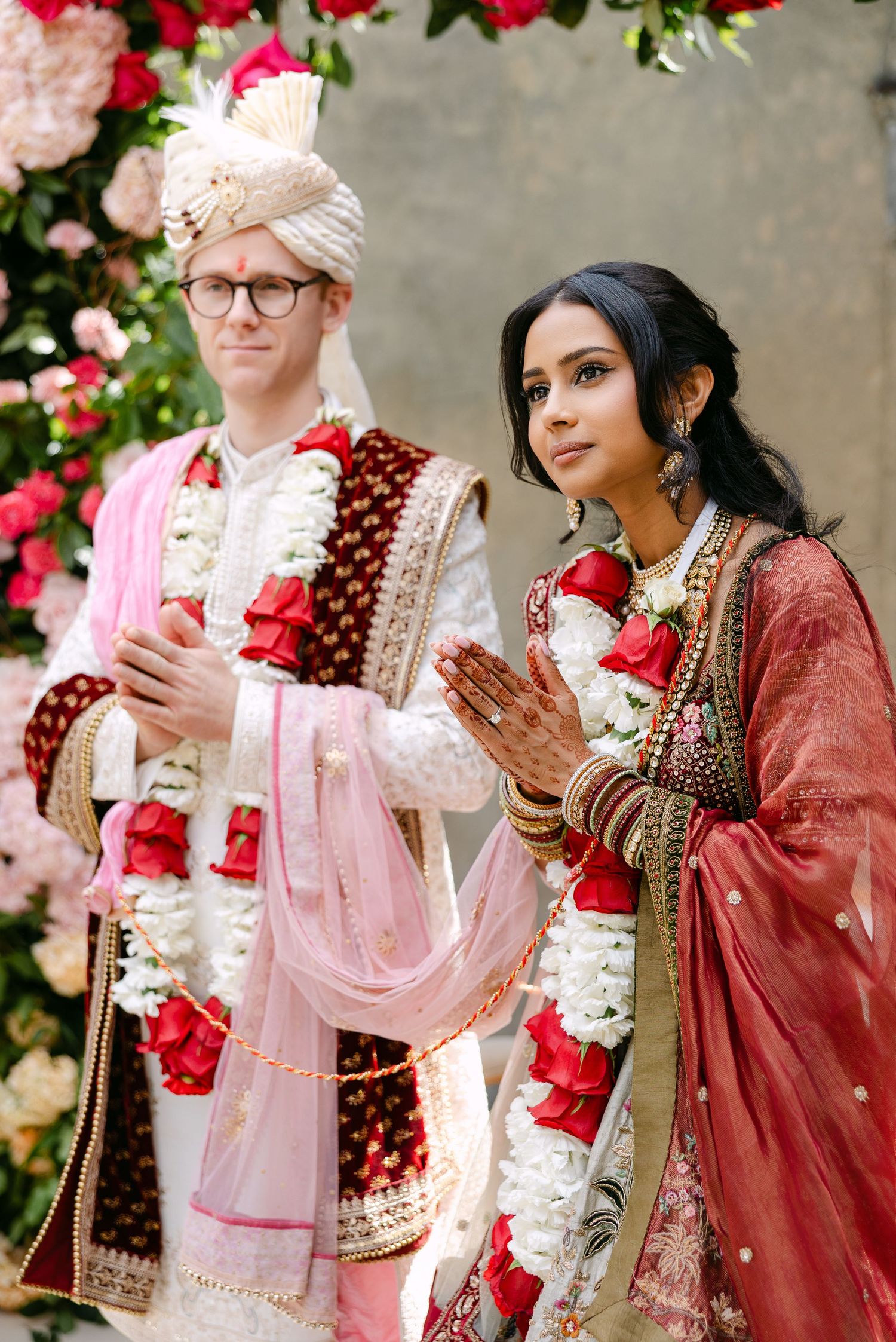 Wedding ceremony participants in traditional Indian and Western attire surrounded by red and pink roses.