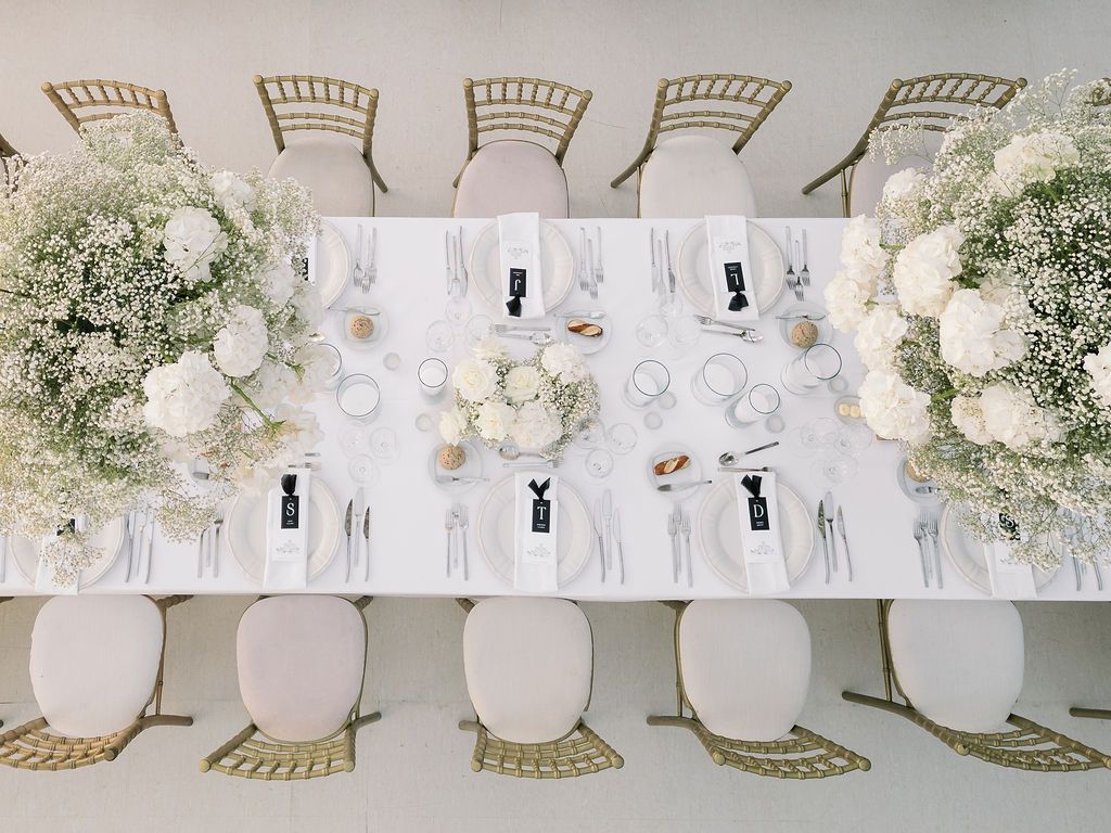 Elegant wedding reception table setting with gold chairs and white floral centerpieces.