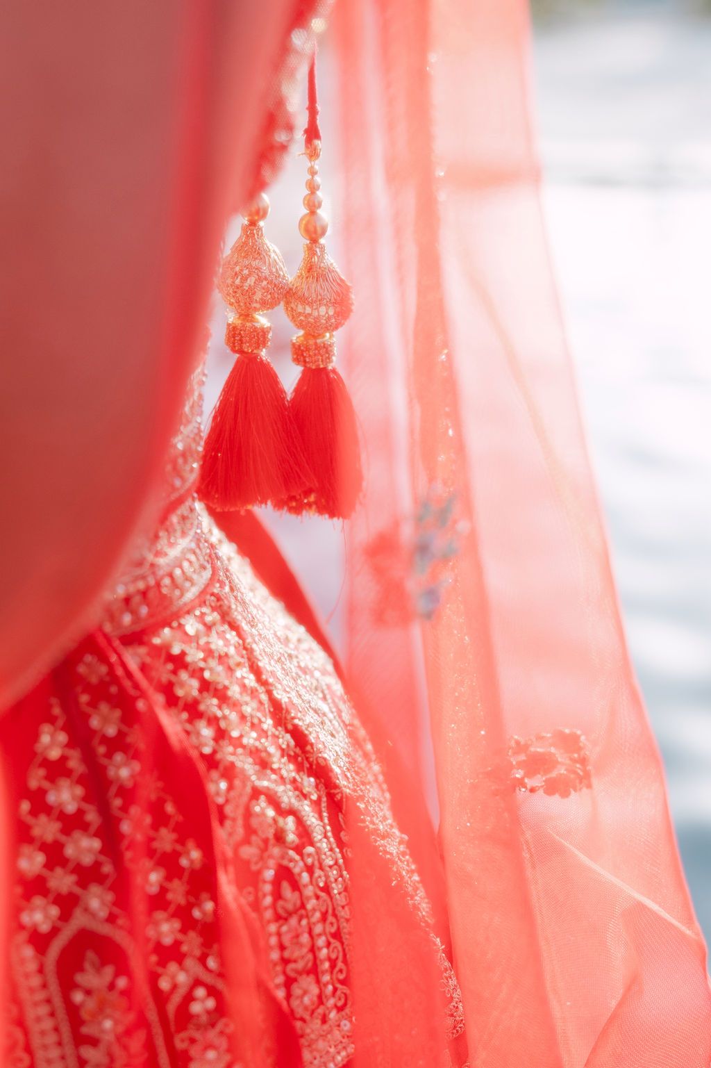 Close-up details of intricate embroidery on red wedding dupatta with soft sunlit glow.