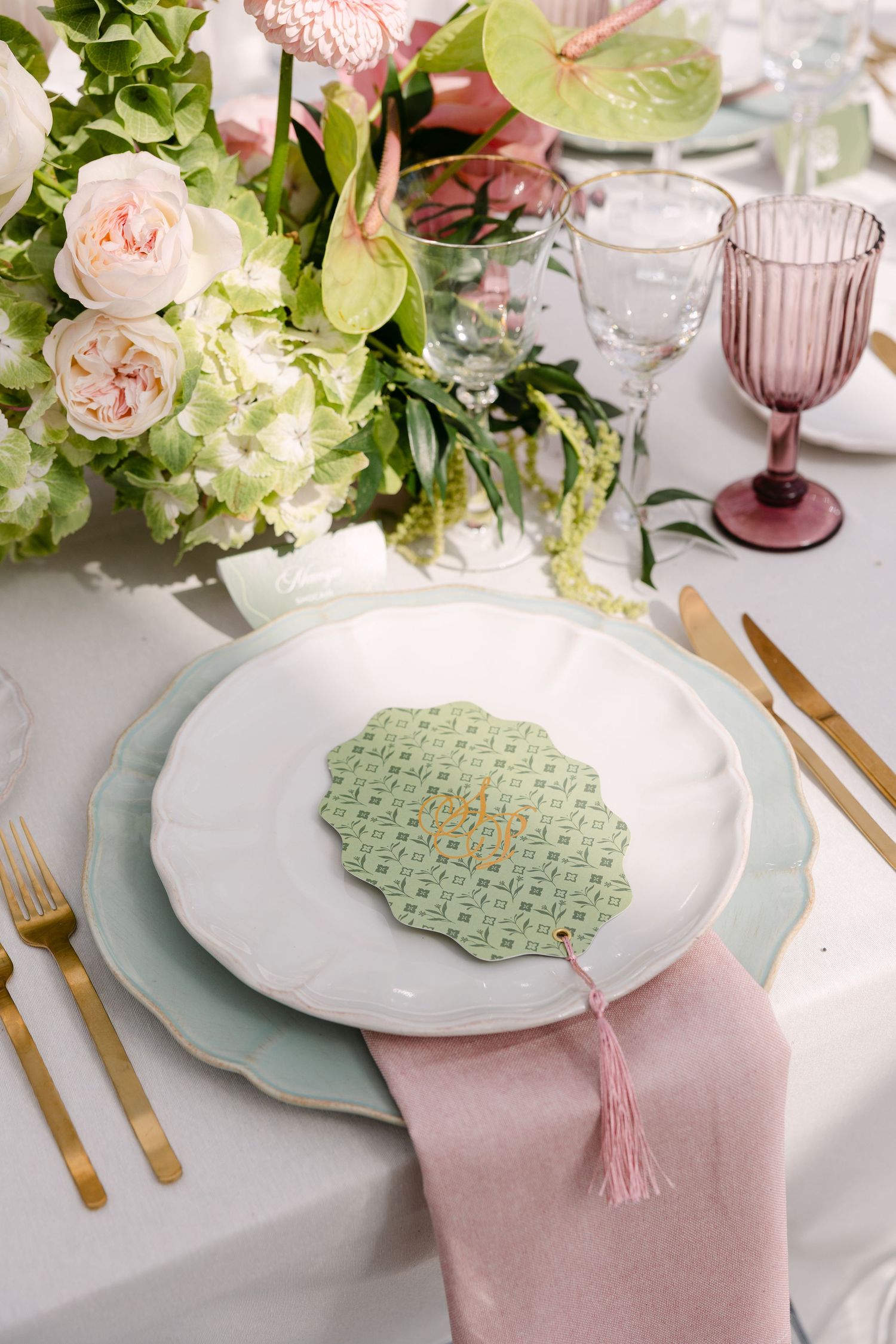Elegant place setting with pink roses, mint green plates, and gold cutlery on a white tablecloth.