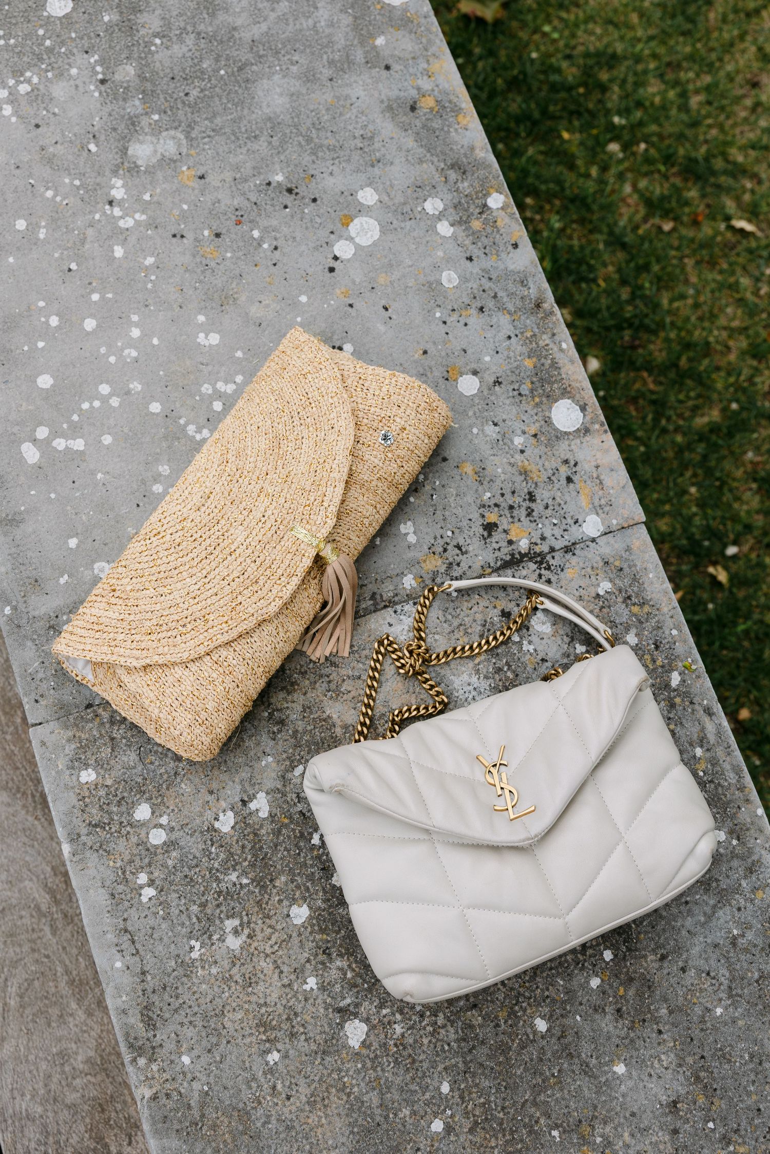 Straw clutch and white YSL designer bag displayed on concrete surface.