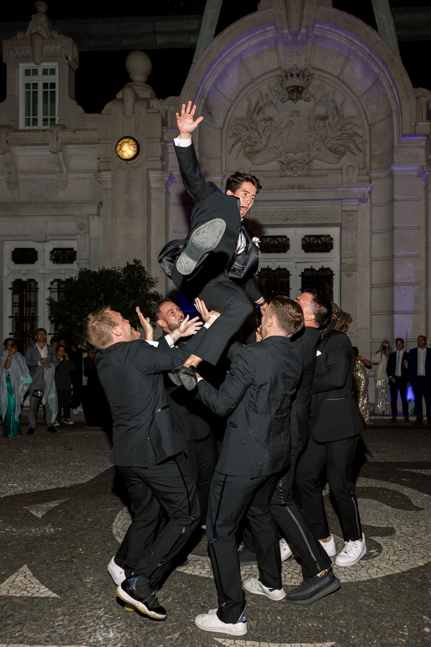 Groomsmen in black suits perform acrobatic moves during wedding reception celebrations.