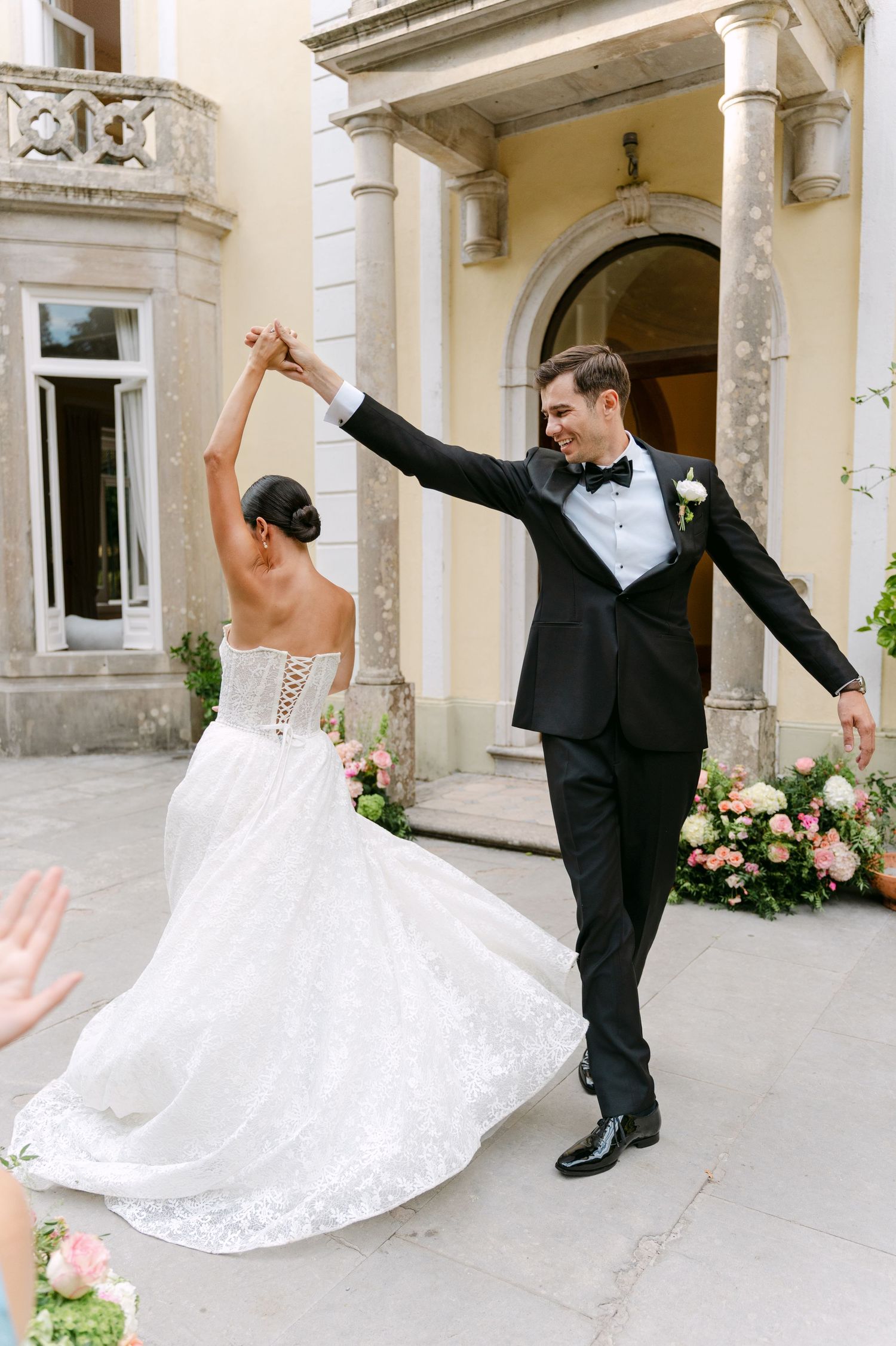 Couple celebrates with joyful dance pose in front of classic architectural entrance.