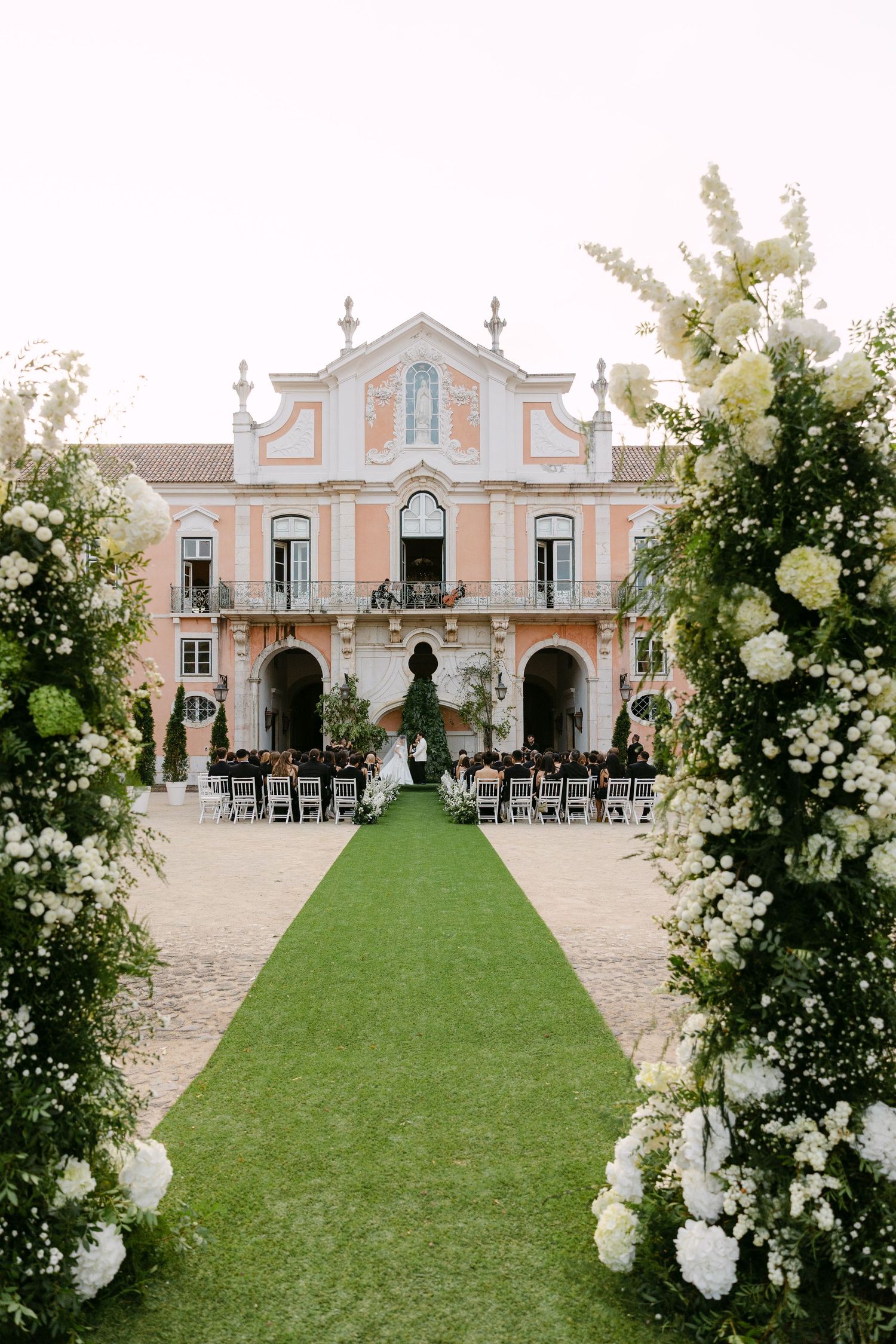 Elegant outdoor wedding ceremony setup with white floral arrangements and chairs on a manicured lawn.