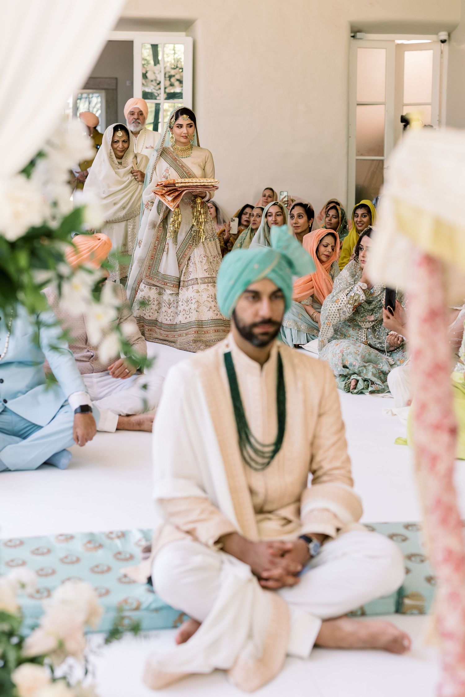 Traditional Sikh wedding ceremony with guests seated on floor in bright, airy venue.