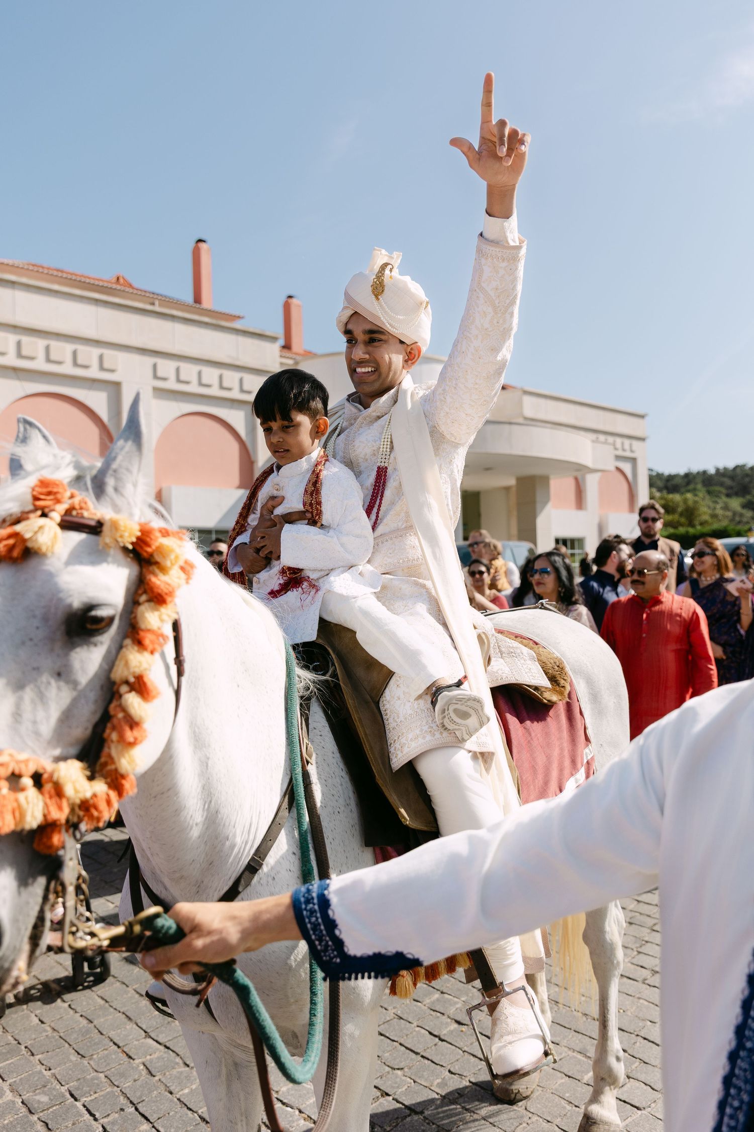 Celebratory dance moves at a wedding with people in white outfits against a pink building backdrop.