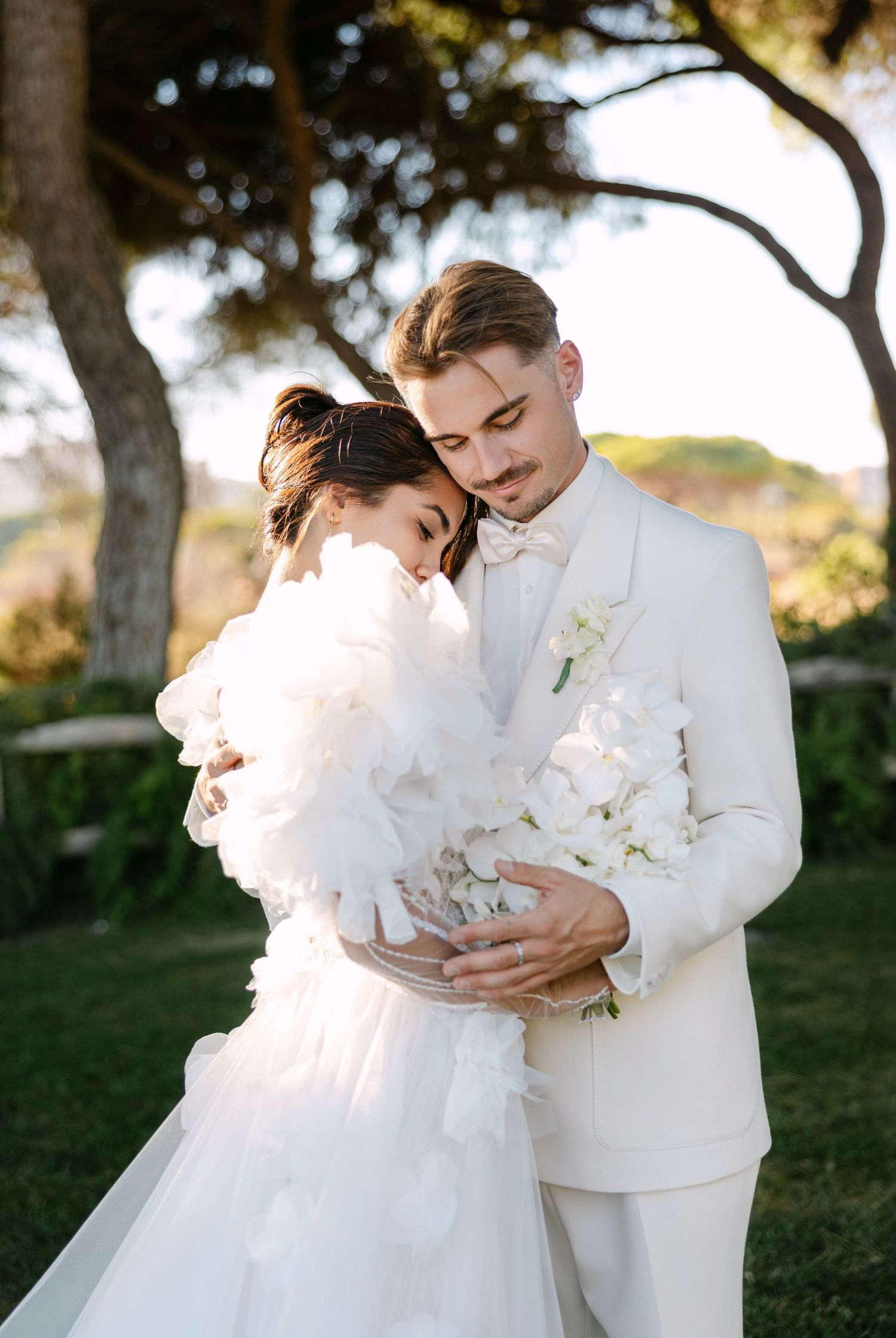Couple embracing in white wedding attire against a garden background.