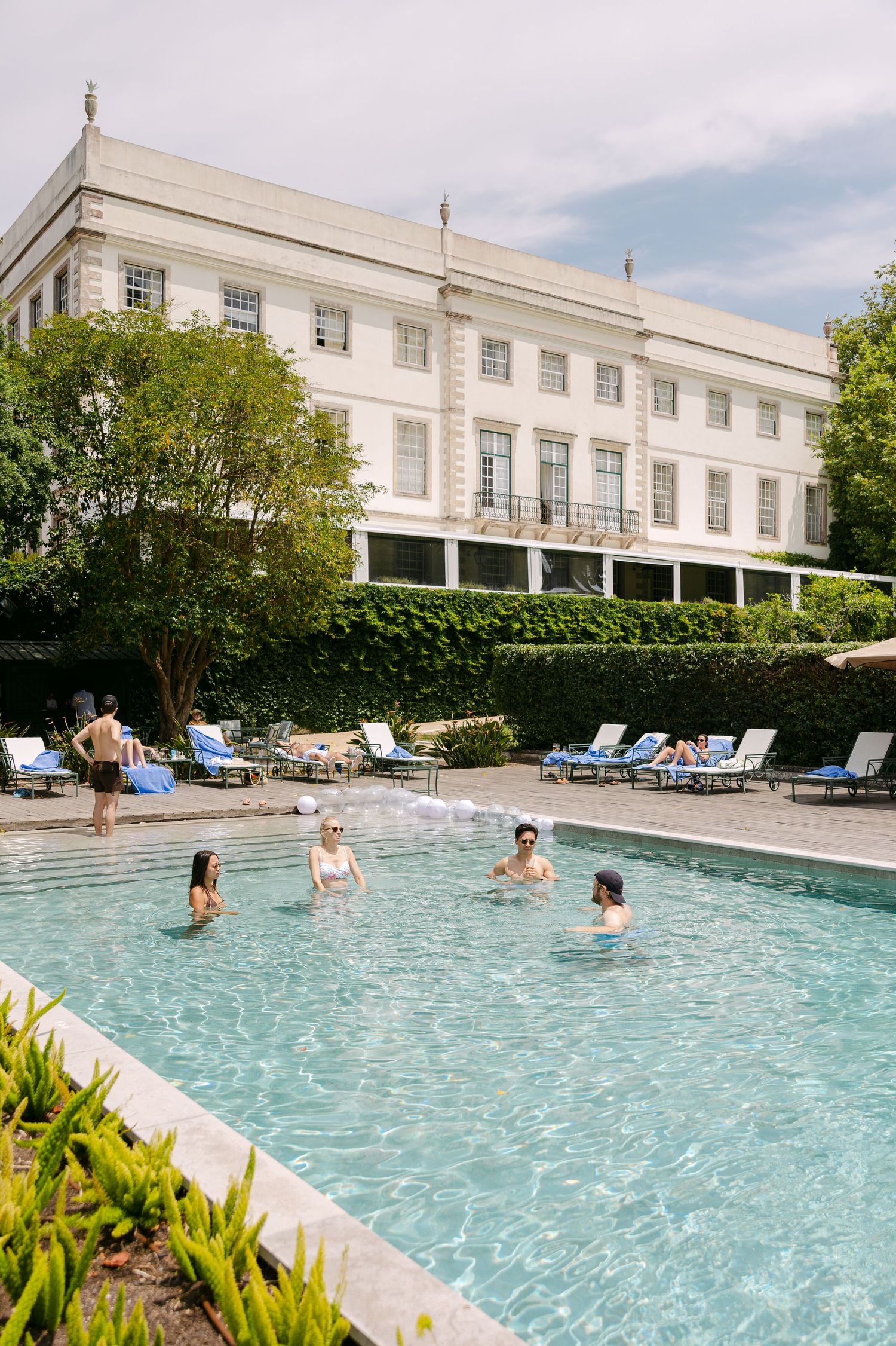 Guests enjoy a luxurious outdoor pool at an elegant white colonial-style resort with lounge chairs and landscaping.