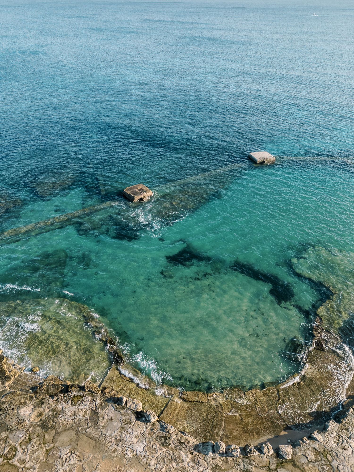 Aerial view of crystal clear turquoise waters meeting rocky coastline.