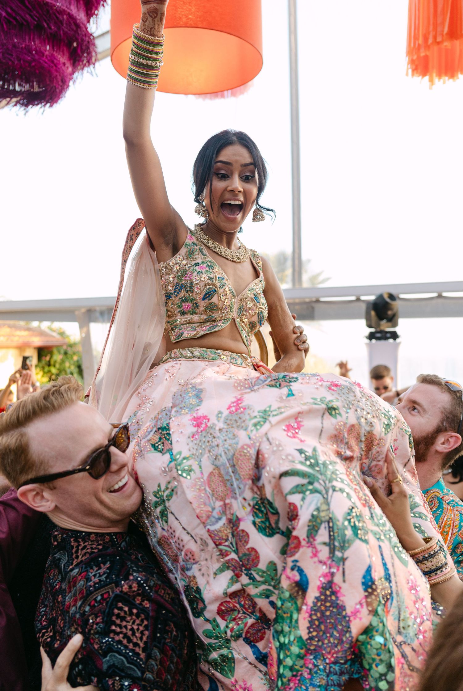 Joyful wedding celebration with guests dancing and laughing in vibrant floral outfits.