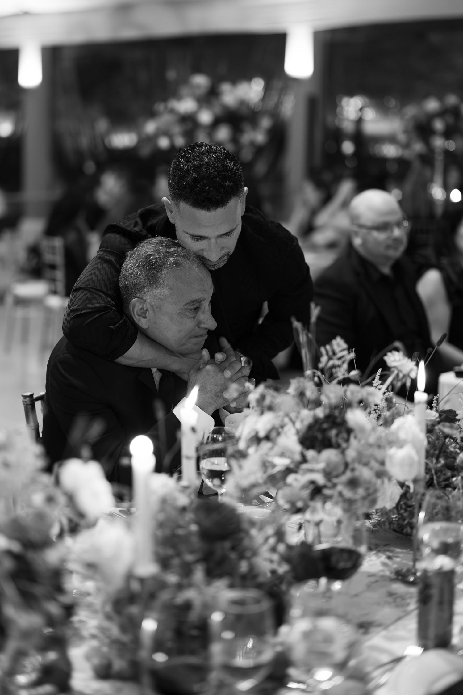 Black and white photo of guests admiring floral centerpieces at dinner table.