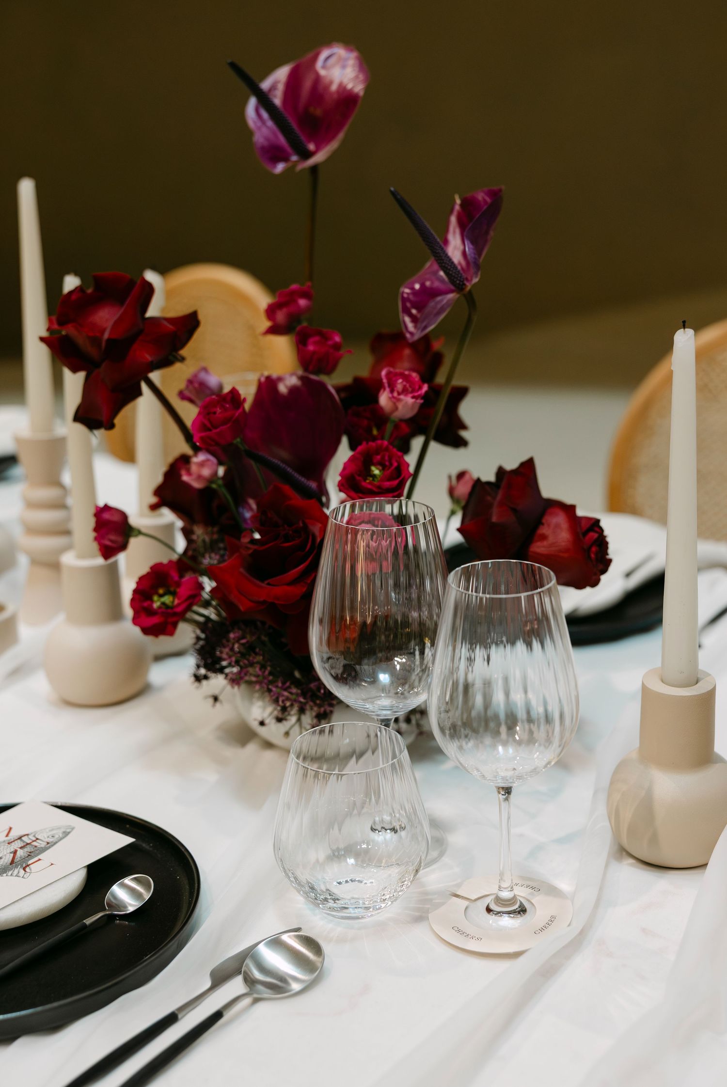 Elegant table setting with deep red floral centerpieces, white candles, and crystal wine glasses.