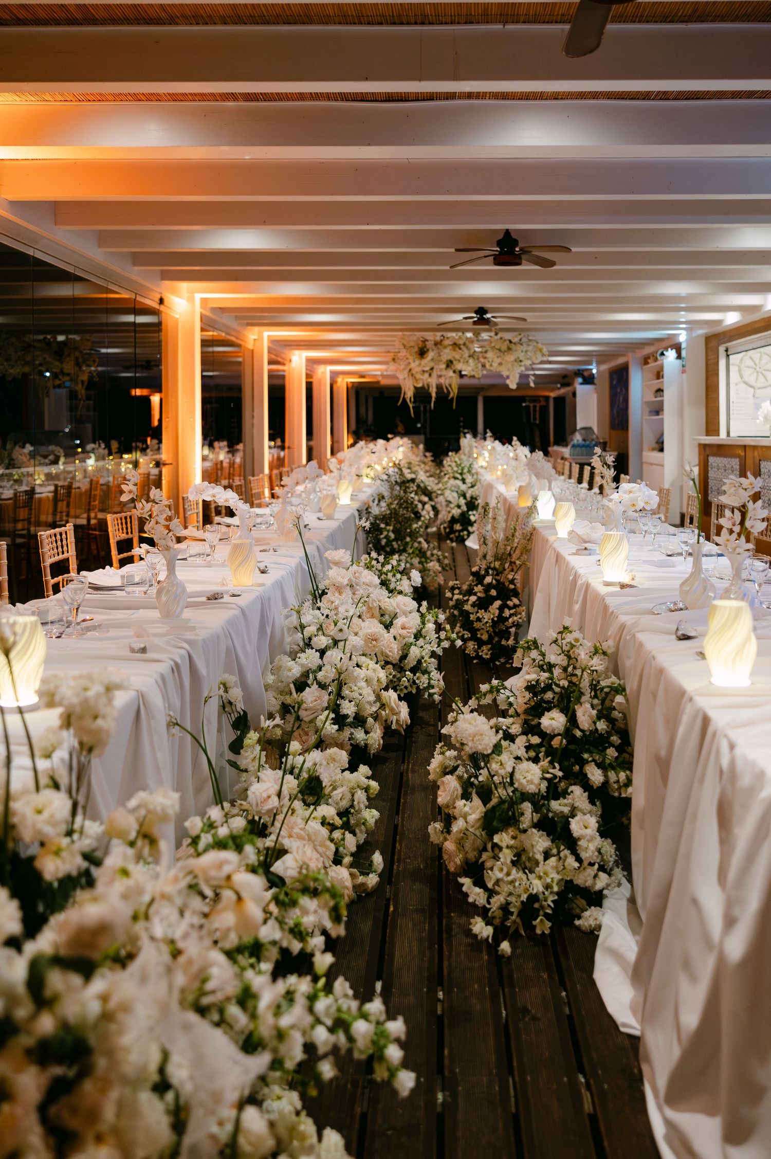 Elegant wedding reception venue with white tablecloths and floral centerpieces illuminated by warm lighting.