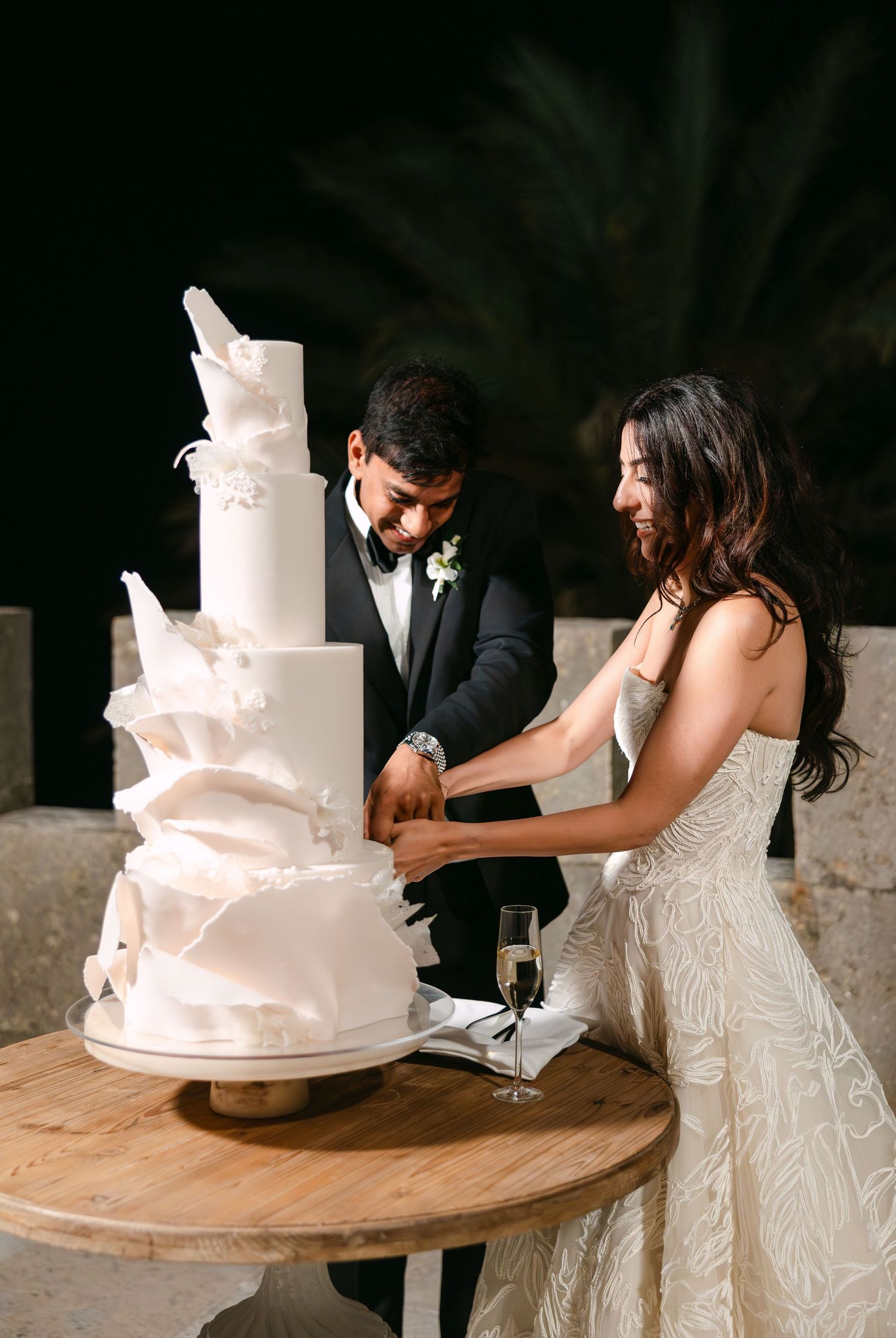 Couple cuts their elegant white wedding cake together during evening reception.
