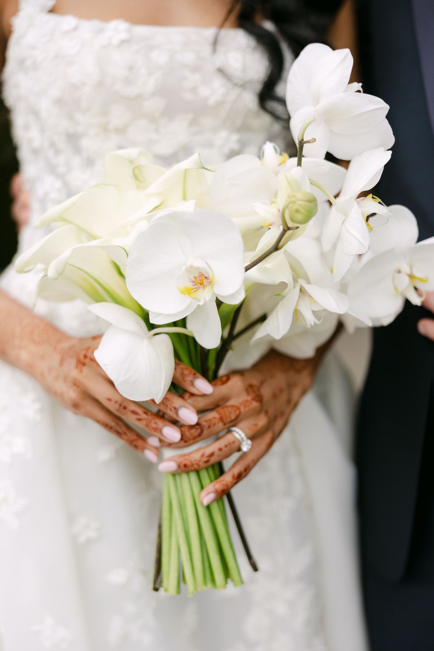 A stunning white orchid bridal bouquet held against a lace wedding dress.