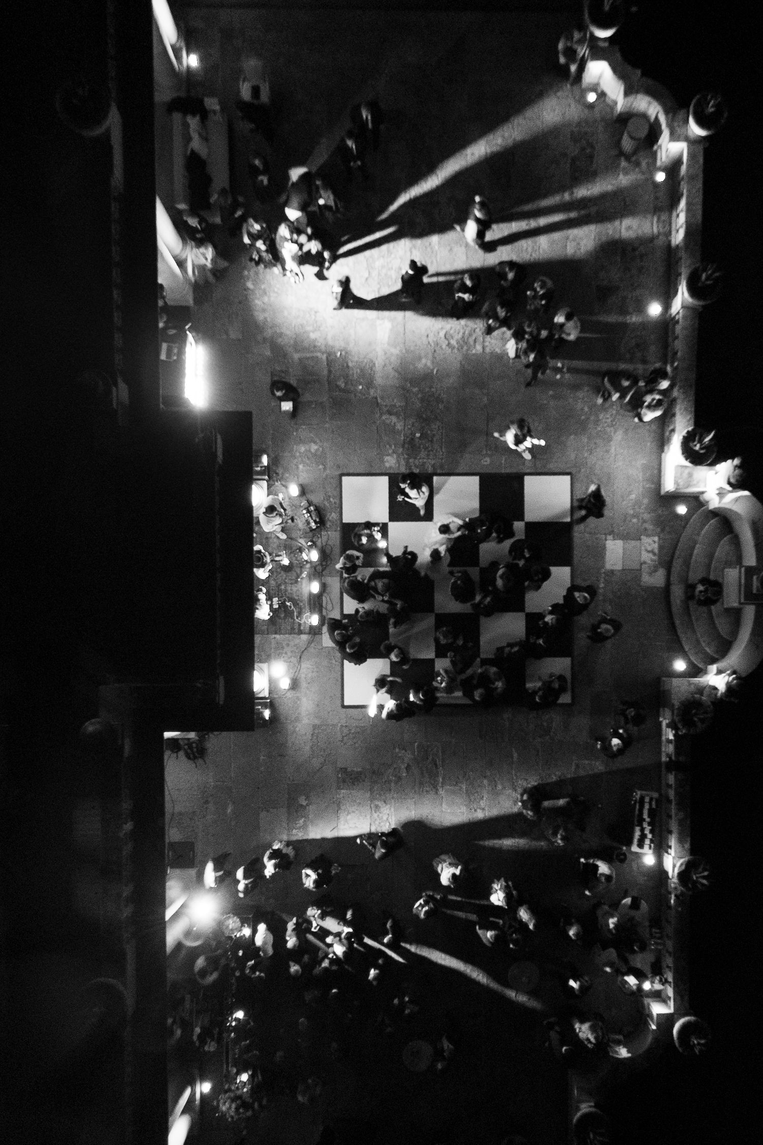 Dramatic aerial black and white photo of wedding guests surrounding a dance floor at a nighttime reception.