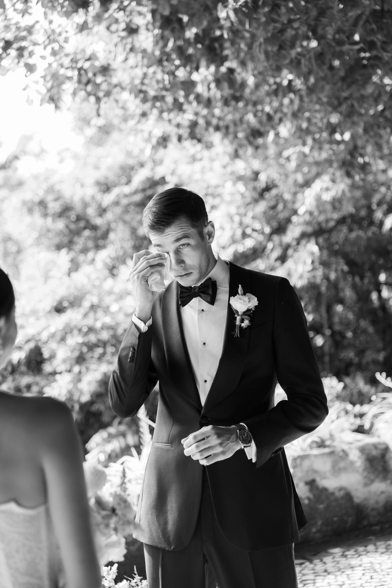Black and white portrait of groom in tuxedo showing emotional reaction outdoors.