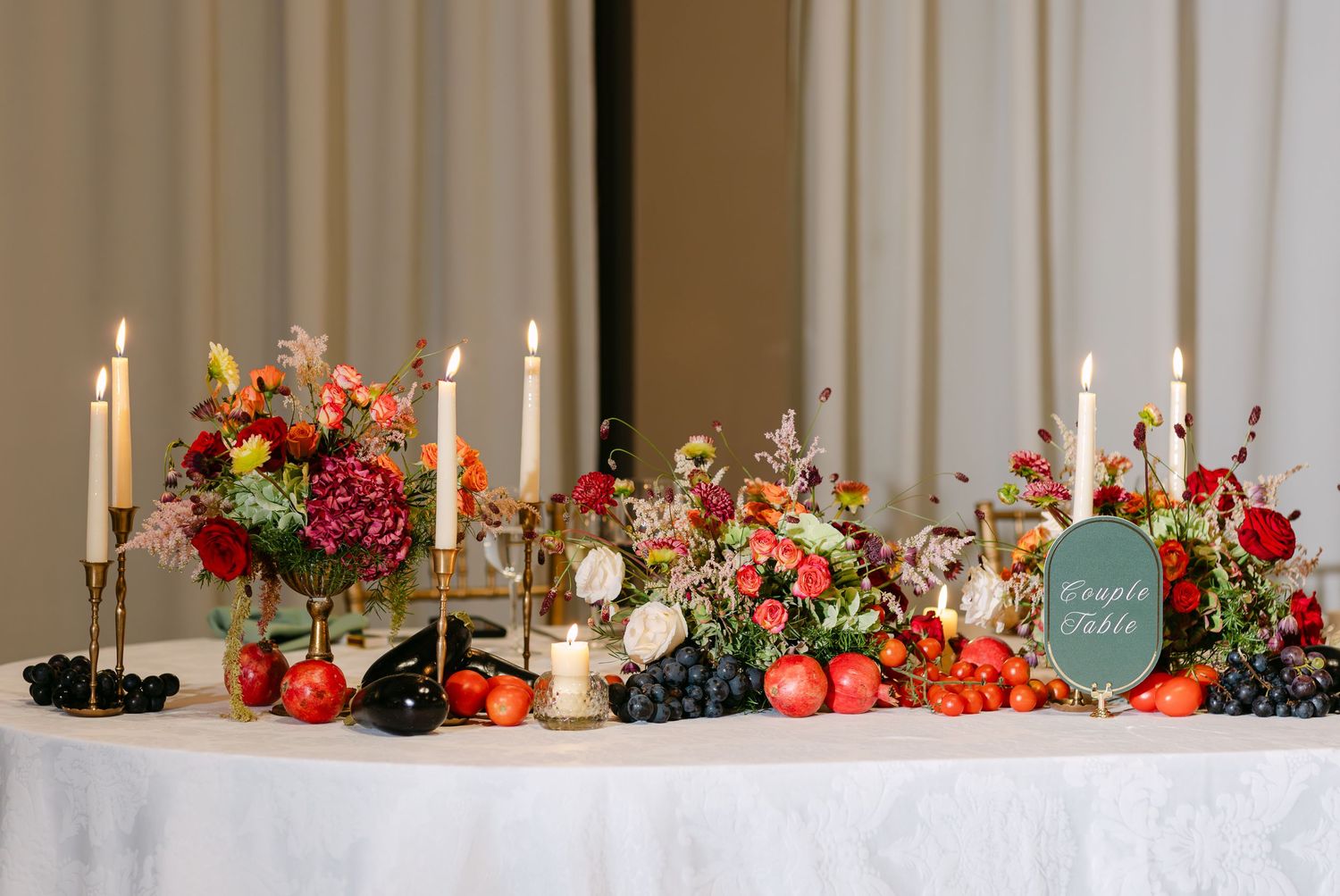 Elegant table setting with red flowers and candles stretching across white tablecloth.