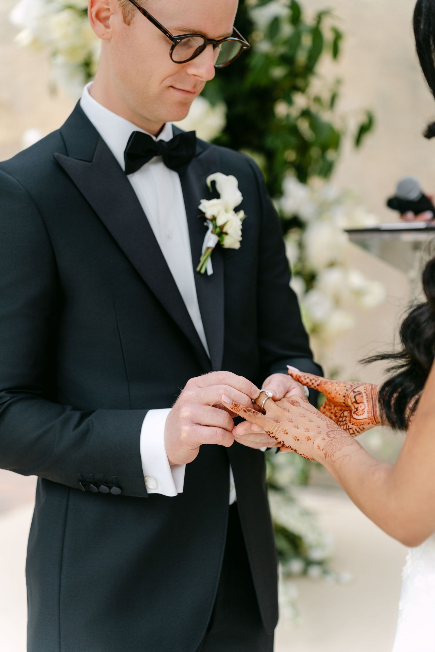 A close-up of a ring exchange during a wedding ceremony with traditional henna-adorned hands.