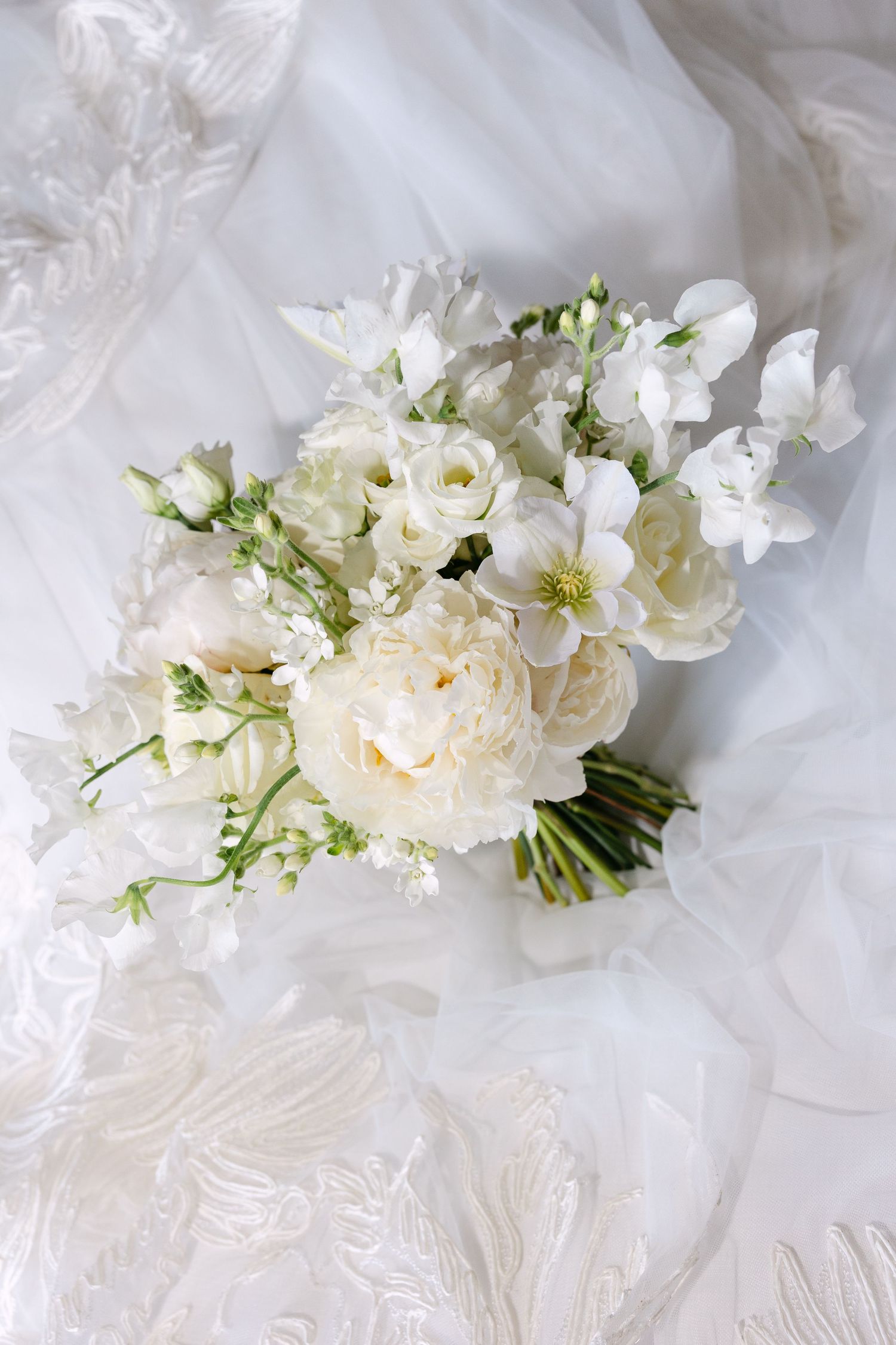Elegant white floral bouquets with roses and delicate greenery arranged on white fabric.