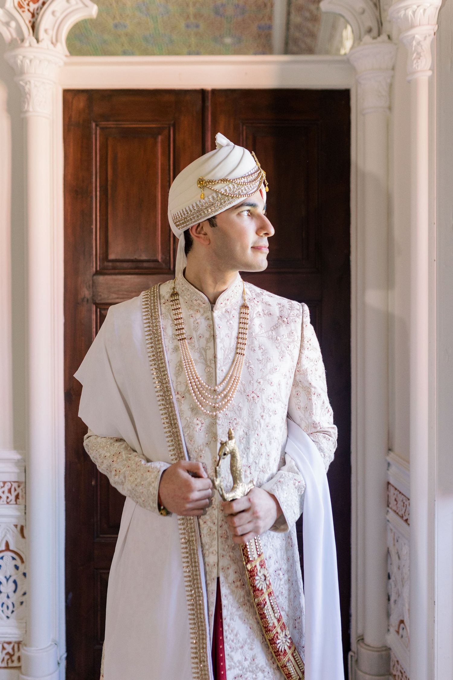Traditional white Indian groom's attire with pearl necklaces displayed in an elegant interior.