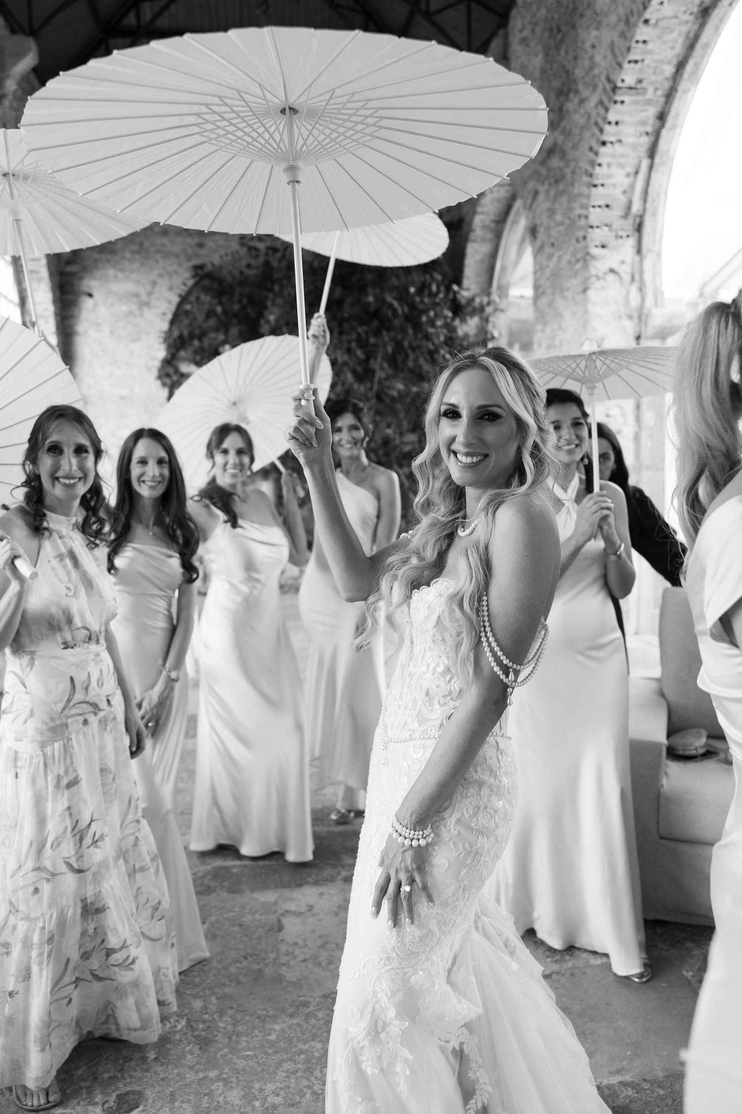 Wedding party poses with white parasols in an elegant outdoor celebration.