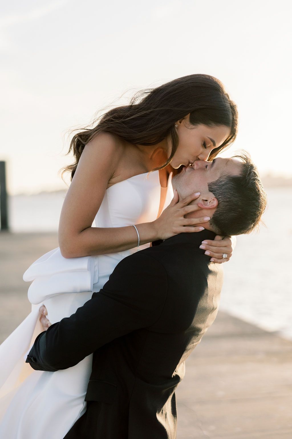 A romantic wedding moment captured at sunset with the couple embracing in formal attire.