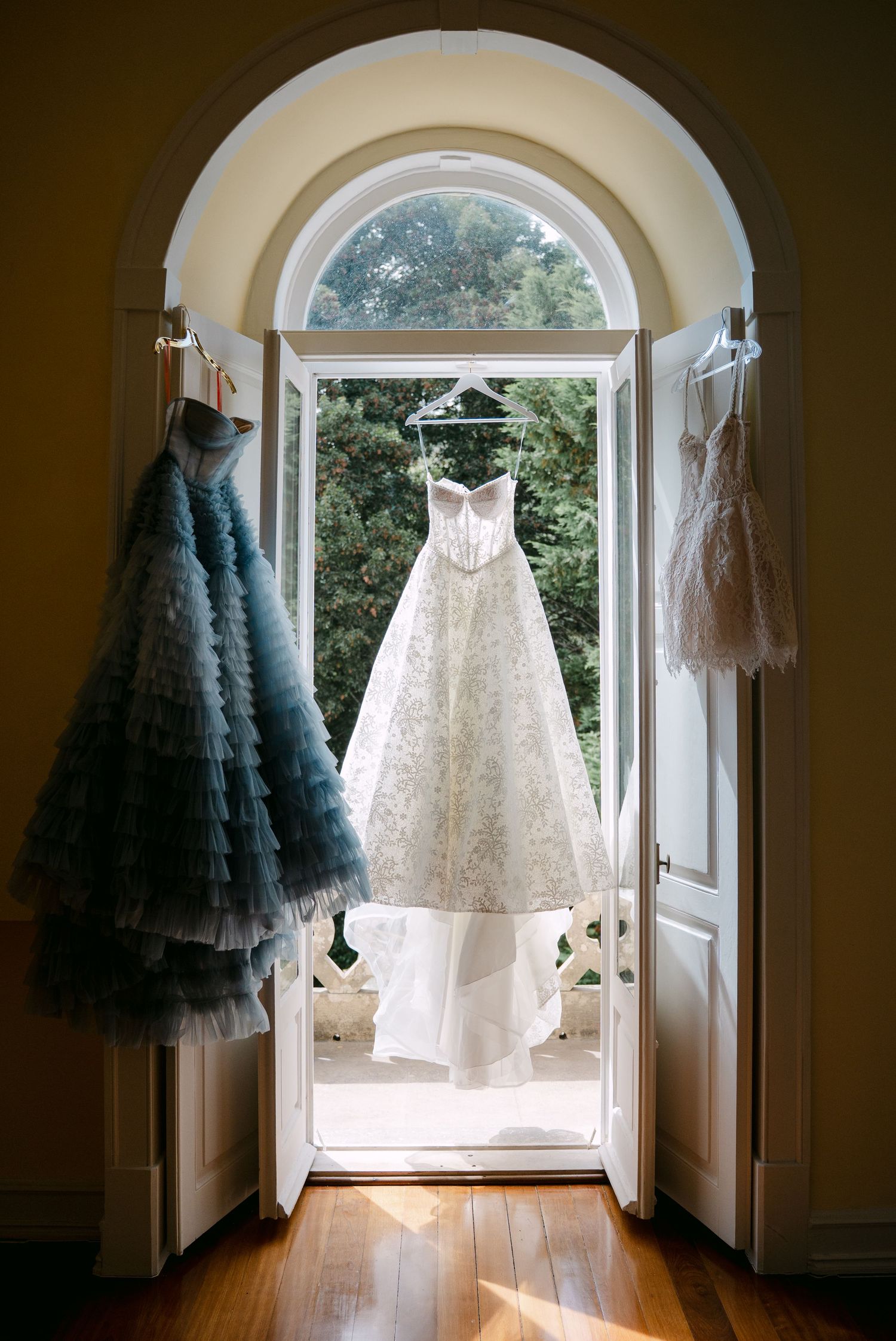 Wedding dresses hanging in arched doorway with natural light streaming through.