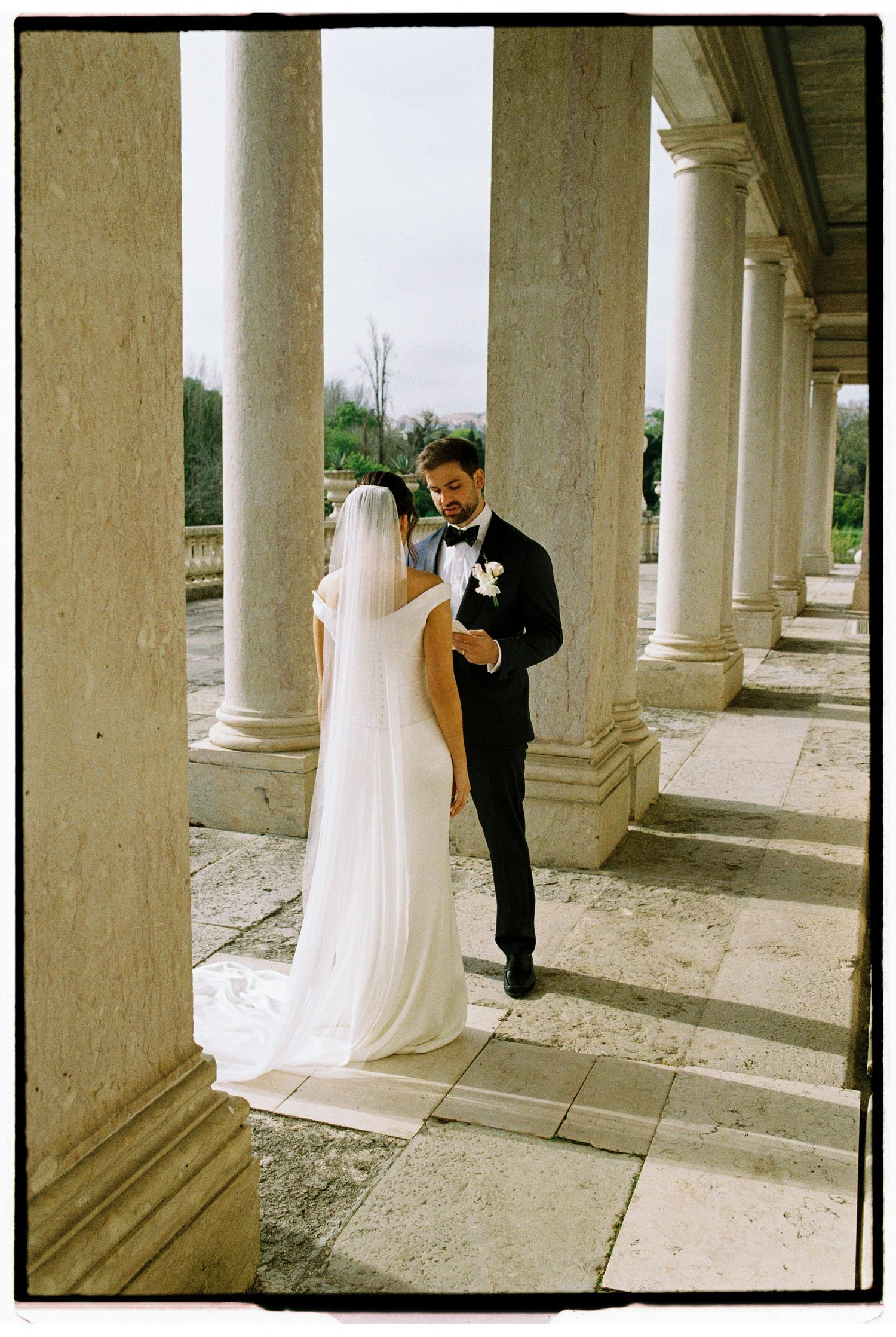 Bride and groom share an intimate moment among marble columns at an elegant European wedding venue.