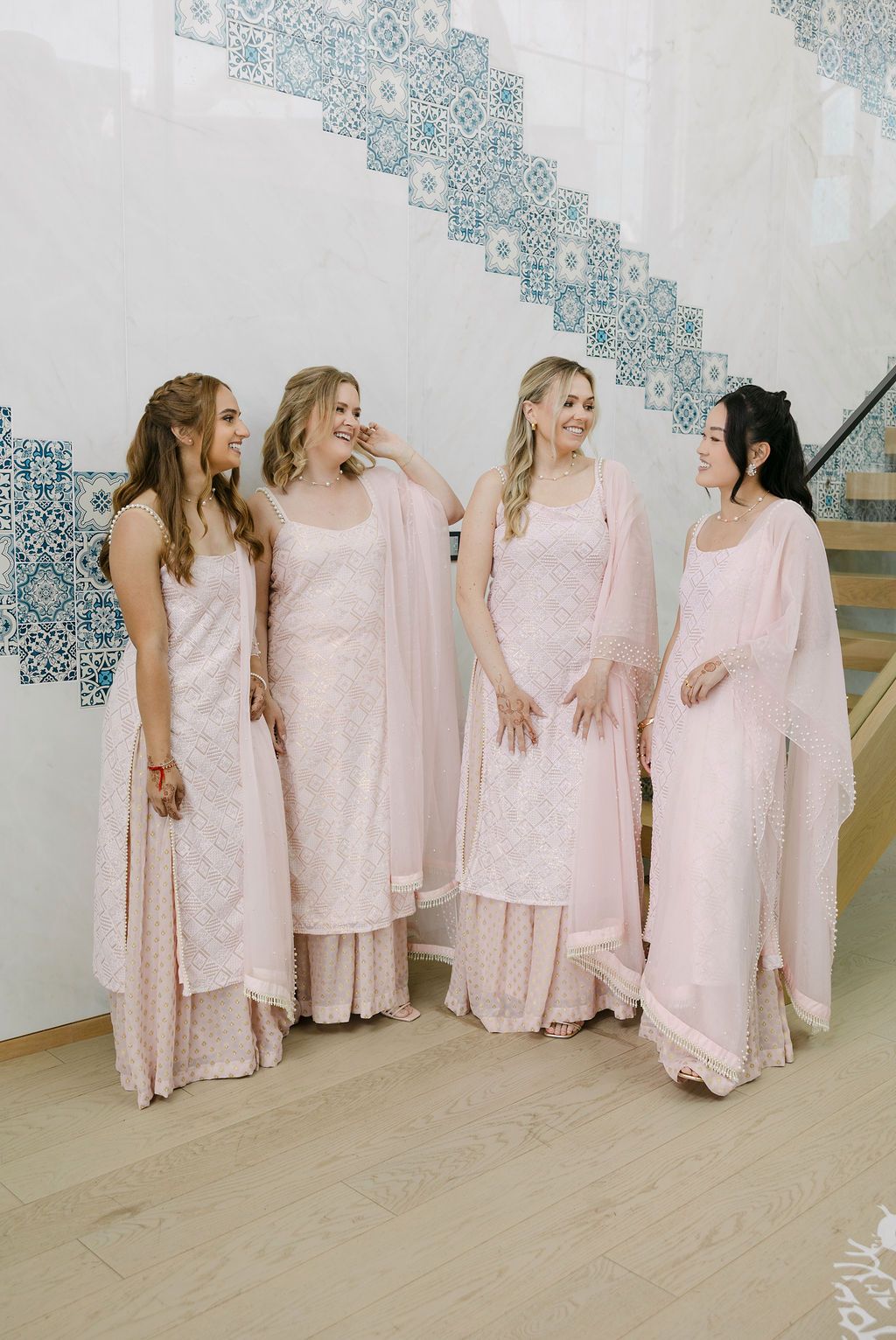 Bridesmaids wearing matching soft pink dresses pose together in an elegant indoor setting.